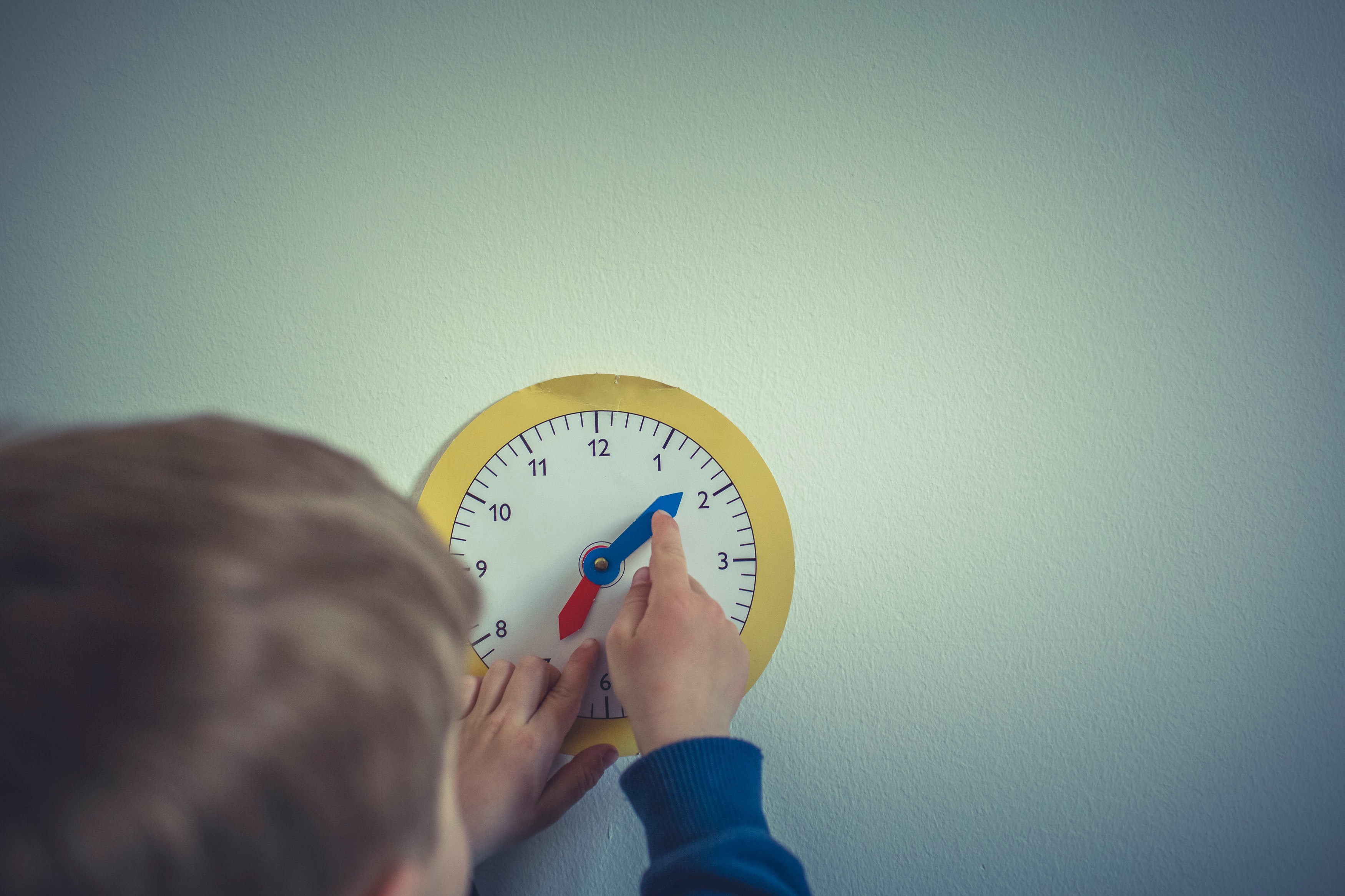 Toddler boy playing with paper clock on wall; image by Markus Spiske, via Unsplash.com.