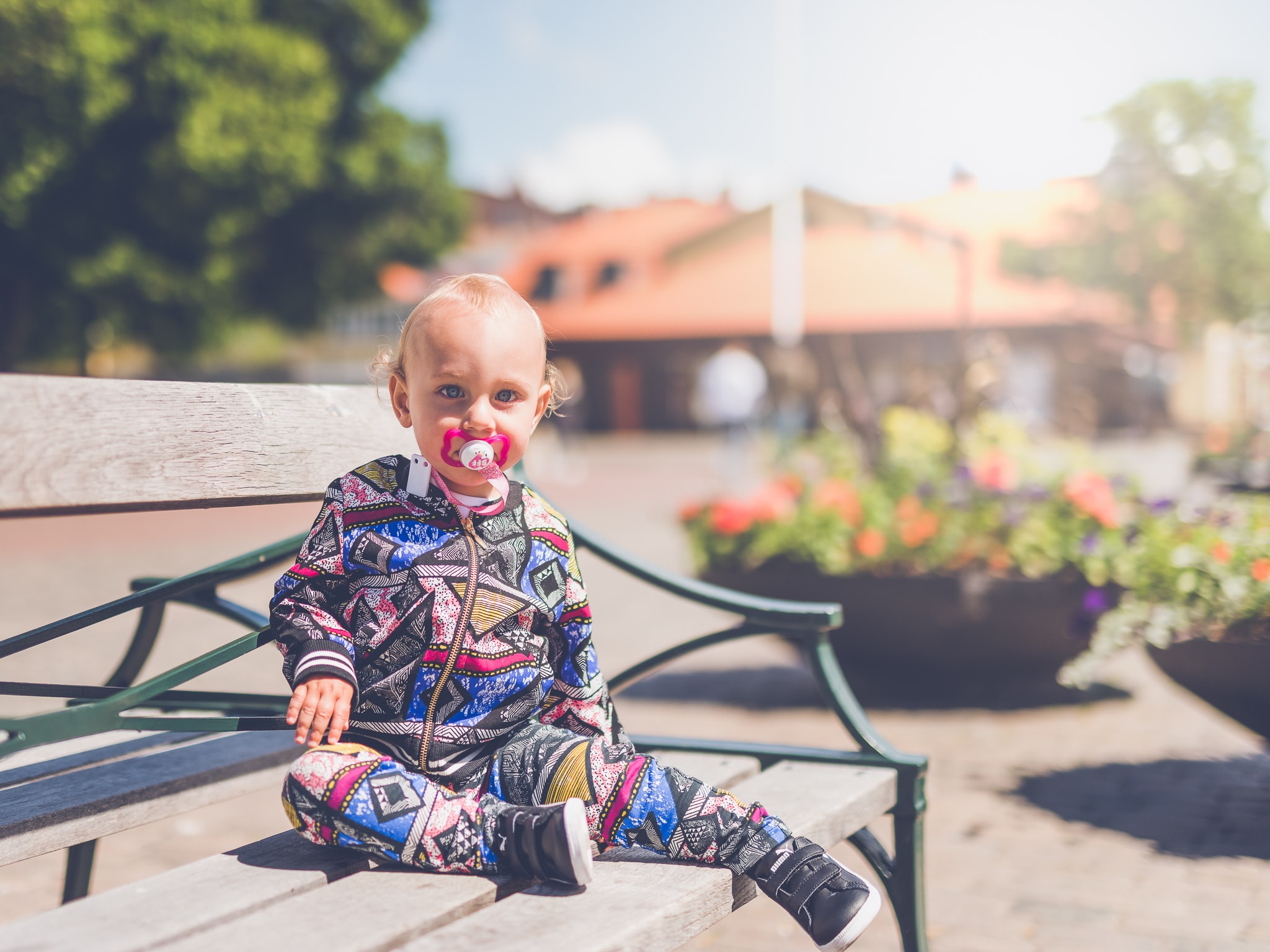 Toddler in colorful pajamas and black tennis shoes sitting on bench; image by Janko Ferlic, via Unsplash.com.