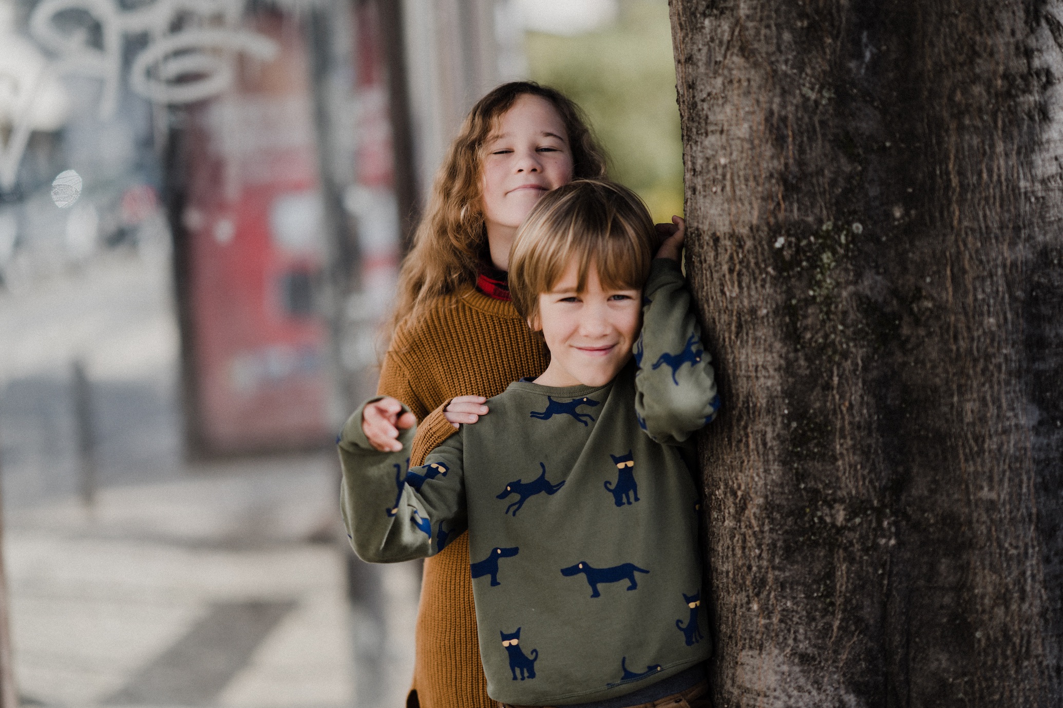 Young boy in sweatshirt and young girl in sweater standing by tree; image by Annie Spratt, via Unsplash.com.