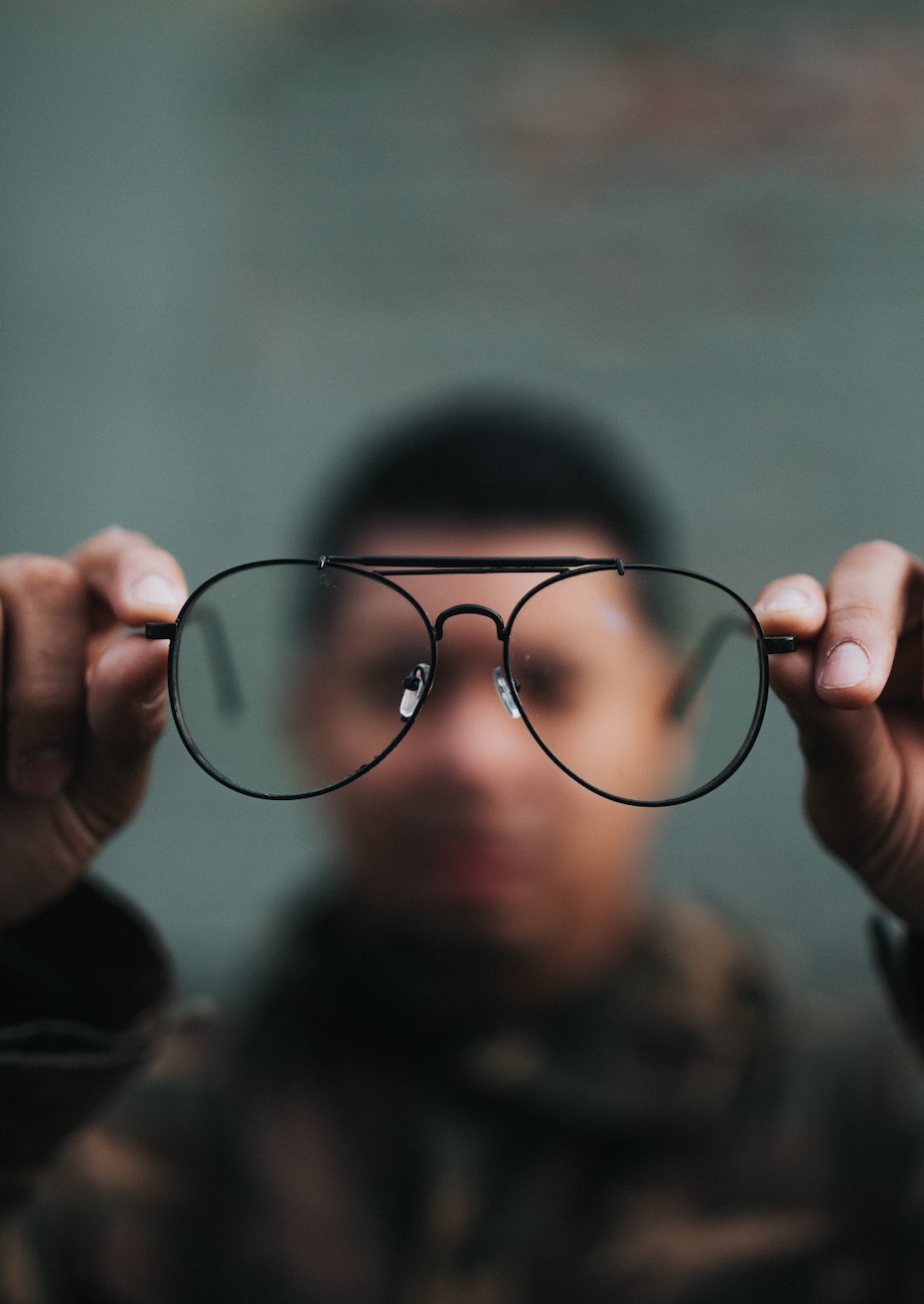 Eyeglasses in perfect focus with man holding them blurred out; image by Nathan Dumlao, via Unsplash.com.