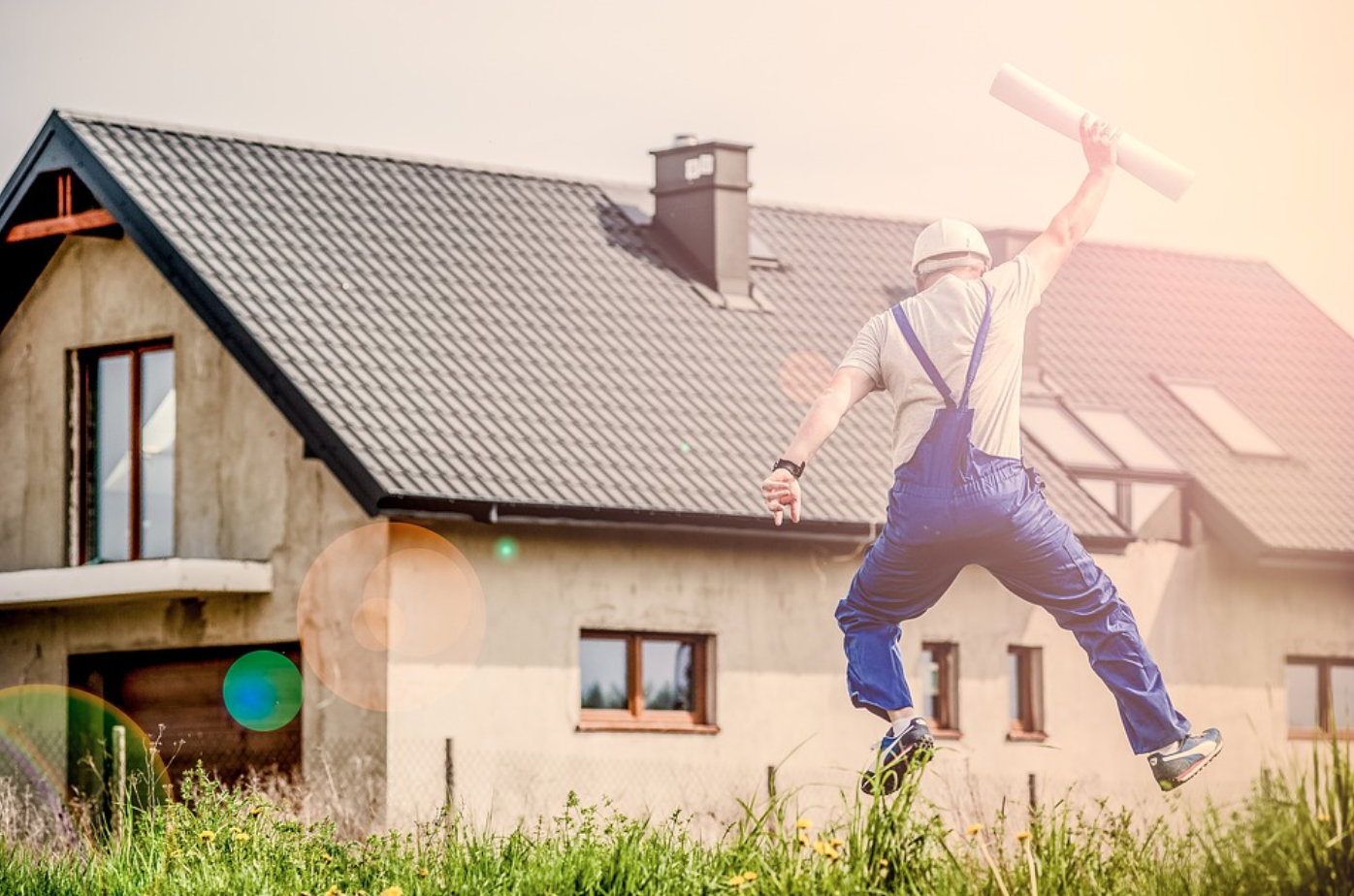Man in overalls holding blueprint and jumping near house; image by Jarmoluk, via Pixabay.com.