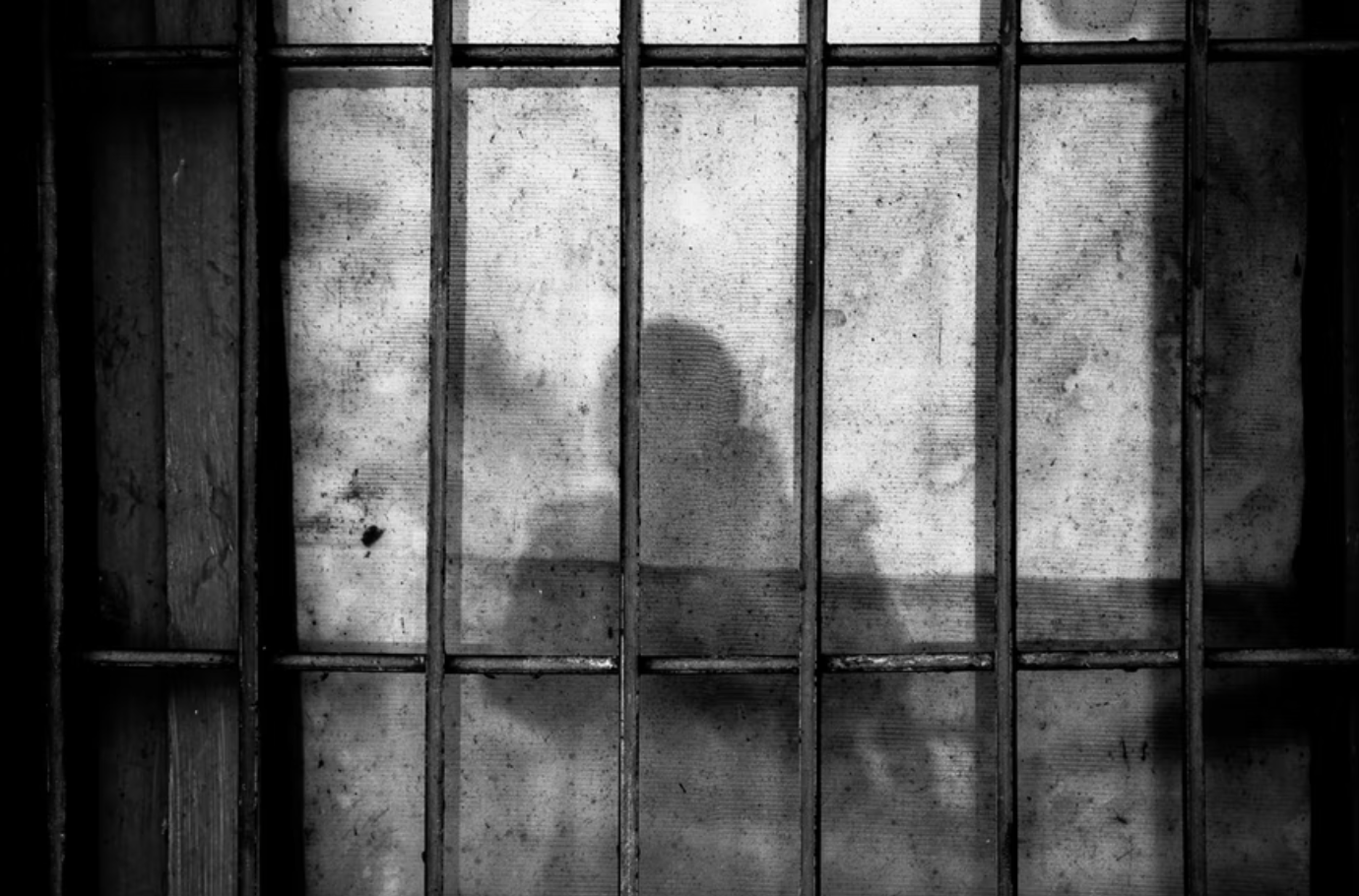 Shadow of person behind bars; image by Ye Jinghan, via Unsplash.com.
