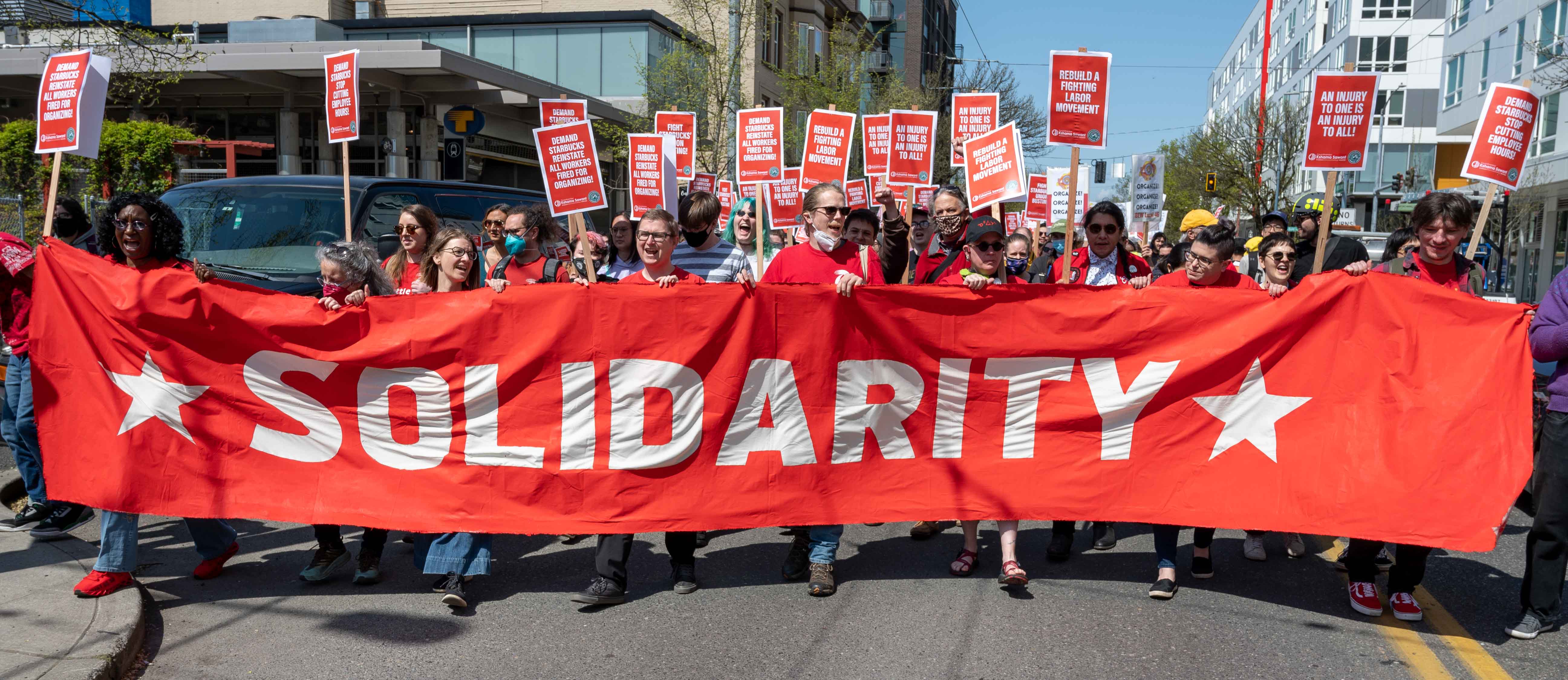 Workers marching behind a large, red sign that says "Solidarity".