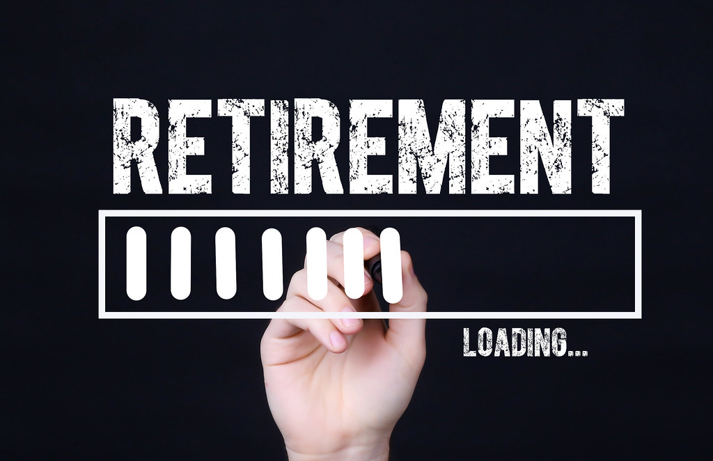A disembodied hand draws a "loading" bar against a dark background, with the word "Retirement" above.