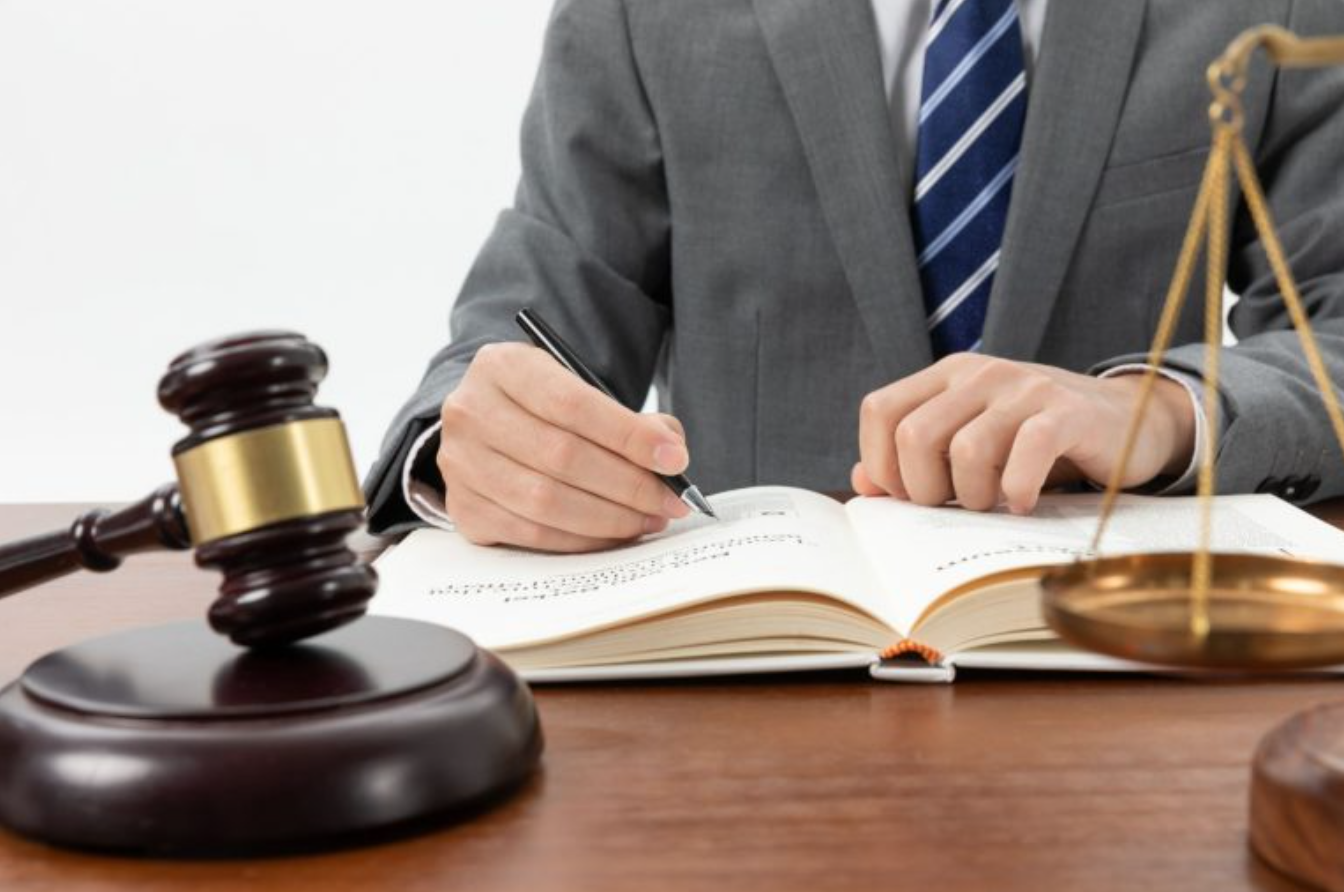 Man in suit writing in book with gavel nearby; image by Wirestock, via Freepik.com.