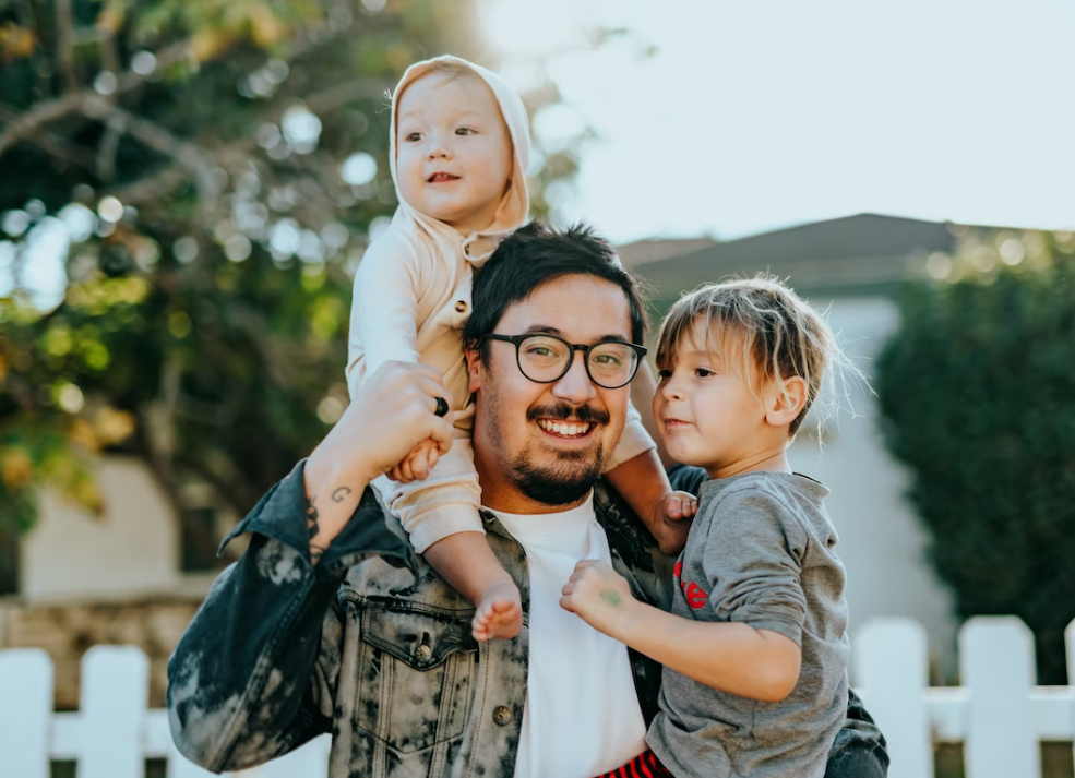 Man in white shirt carrying children; image by Nathan Dumlao, via Unsplash.com.