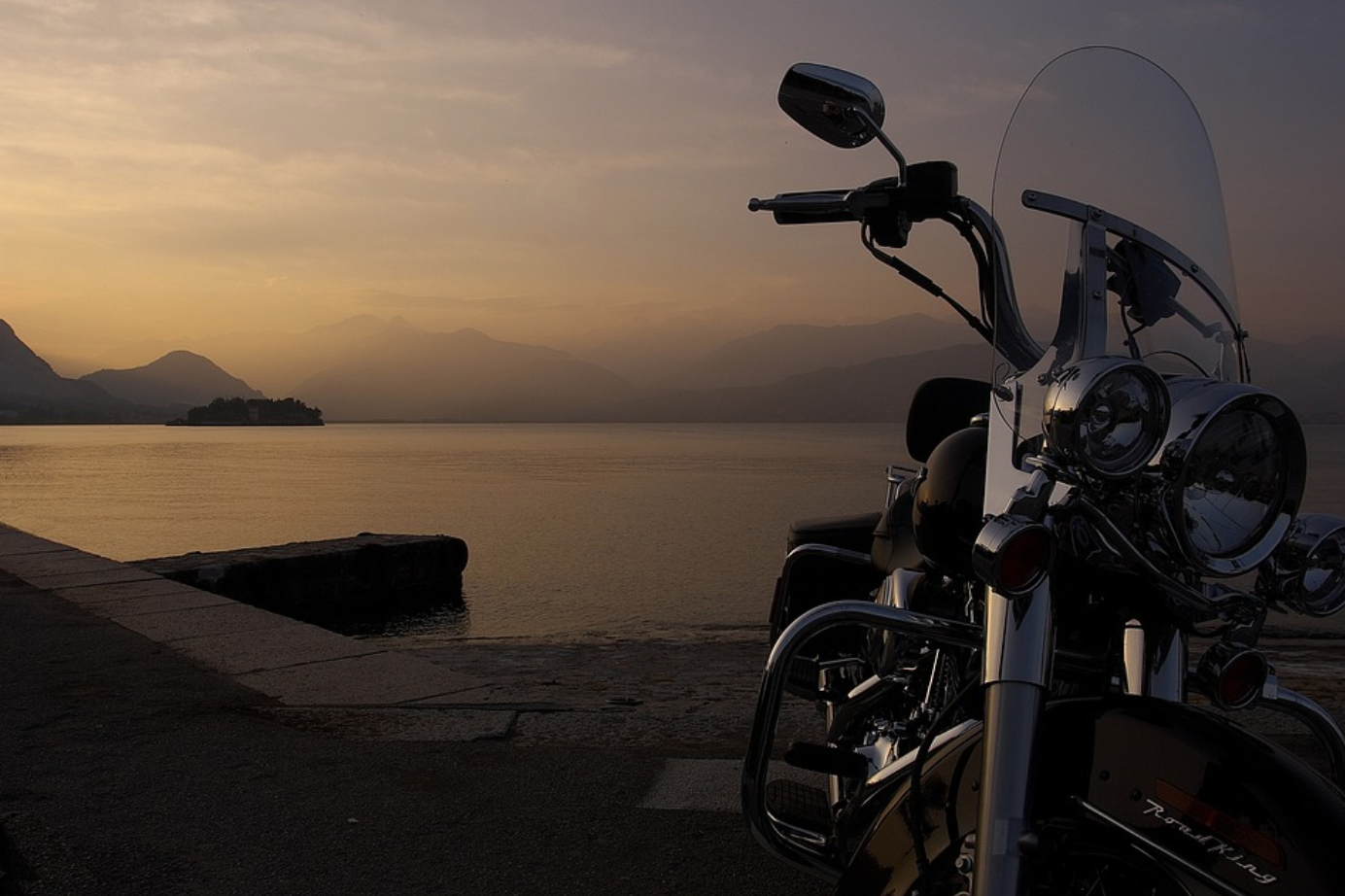 Motorcycle parked by lake; image by Scozzy, via Pixabay.com.