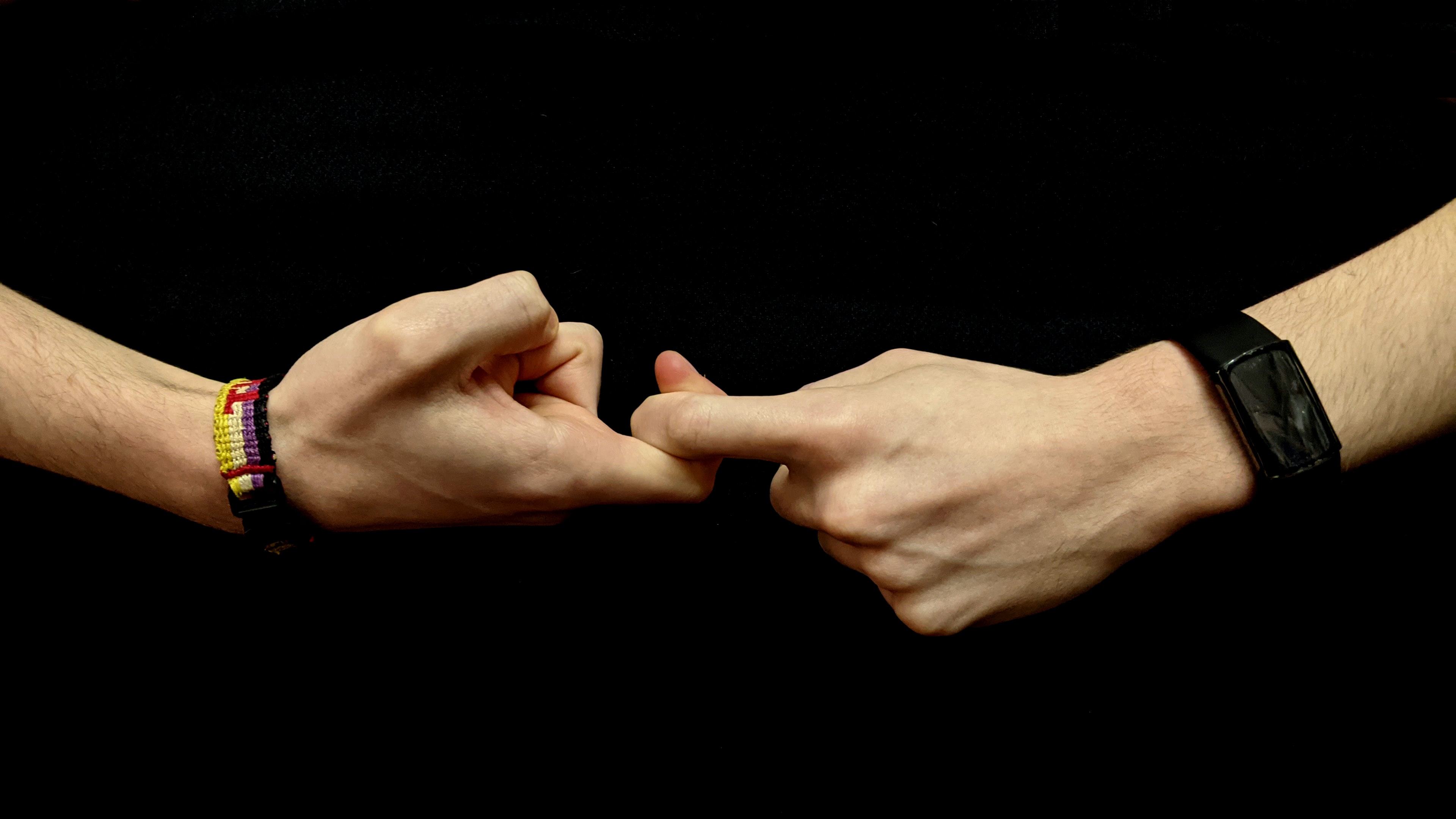 The hands of a young white person against a black background form the first half of the sign for “friendship” in American Sign Language. Image by Nic Rosenau, via Unsplash.com.