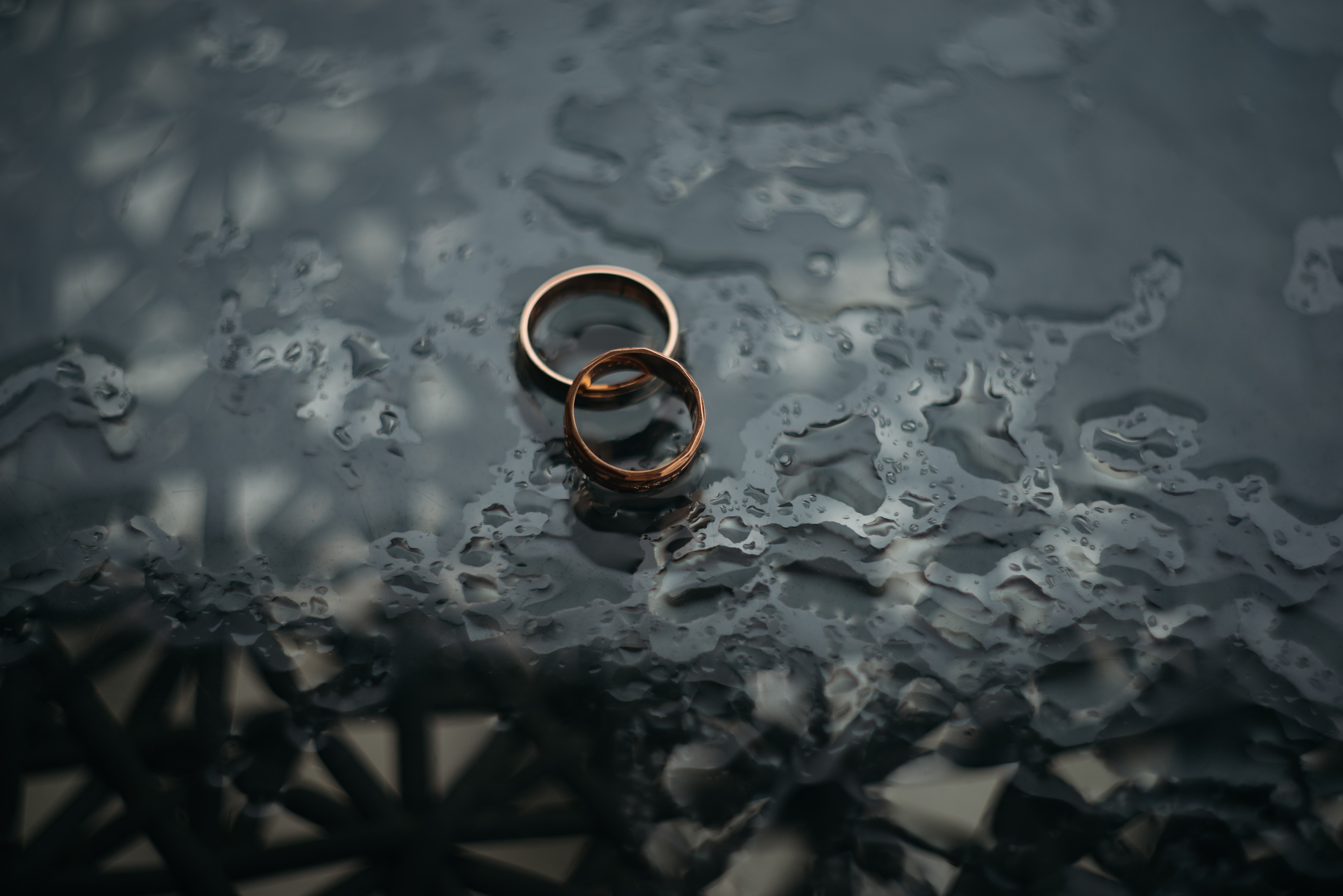 Two wedding rings on dark, wet surface; image by Zoriana Stakhniv, via Unsplash.com.