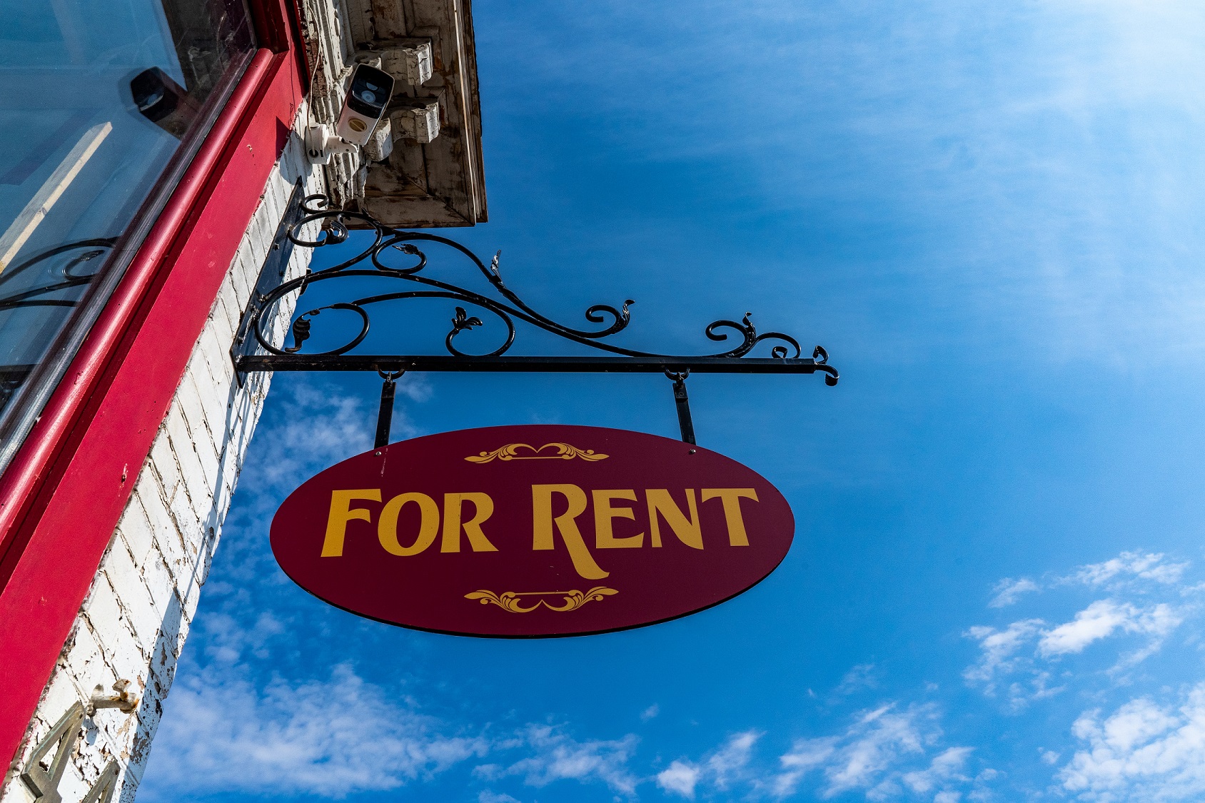 The side of a building with a "for rent" sign hanging against a clear blue sky.