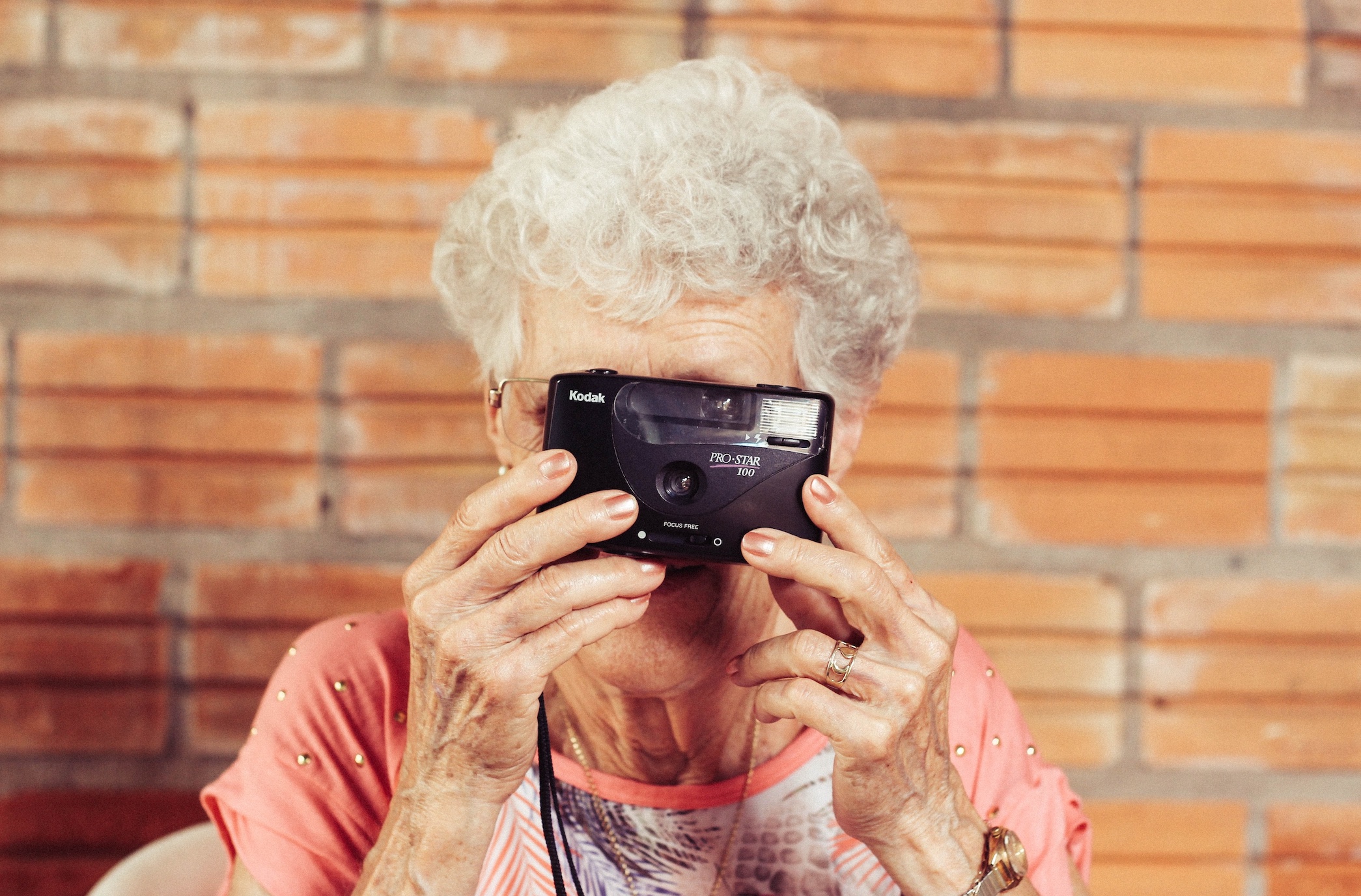 Elderly woman taking picture with camera; image by Tiago Muraro, via Unsplash.com.