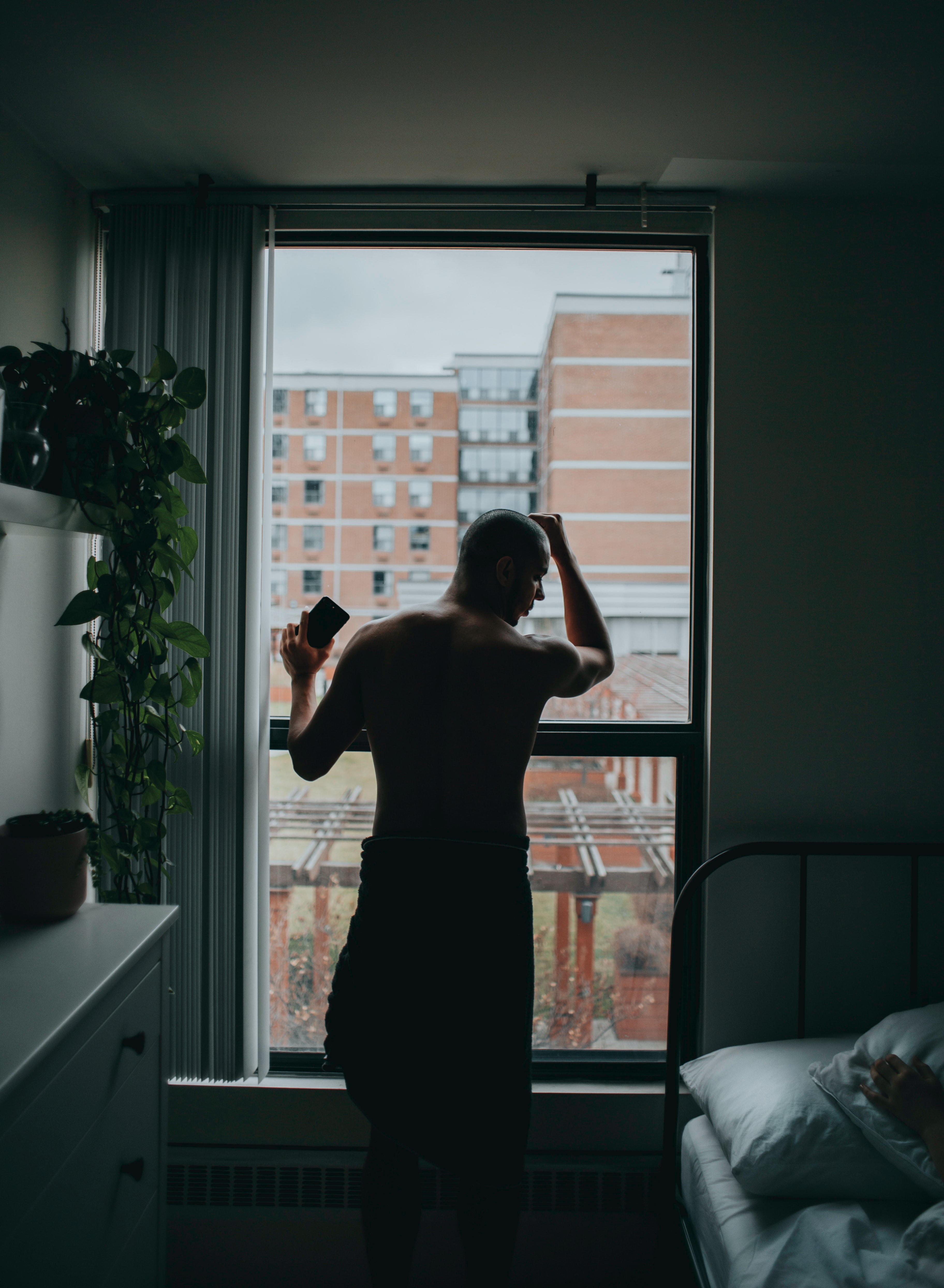 Man standing by bed near window; image by Marcos Paulo Prado, via Unsplash.com.