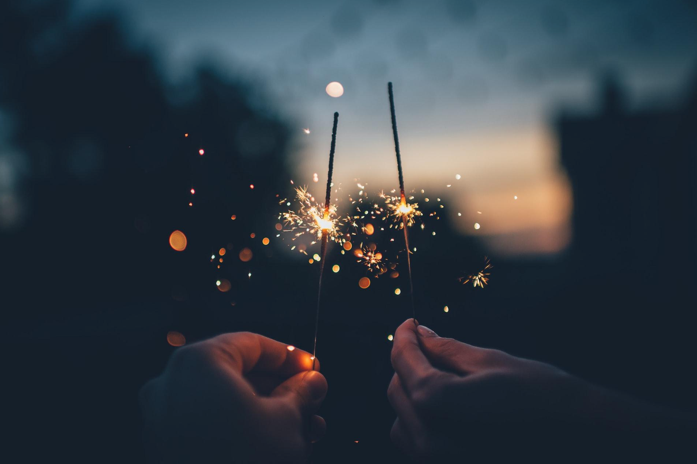 Two people holding lit sparklers in the dark; image by Ian Schneider, via Unsplash.com.