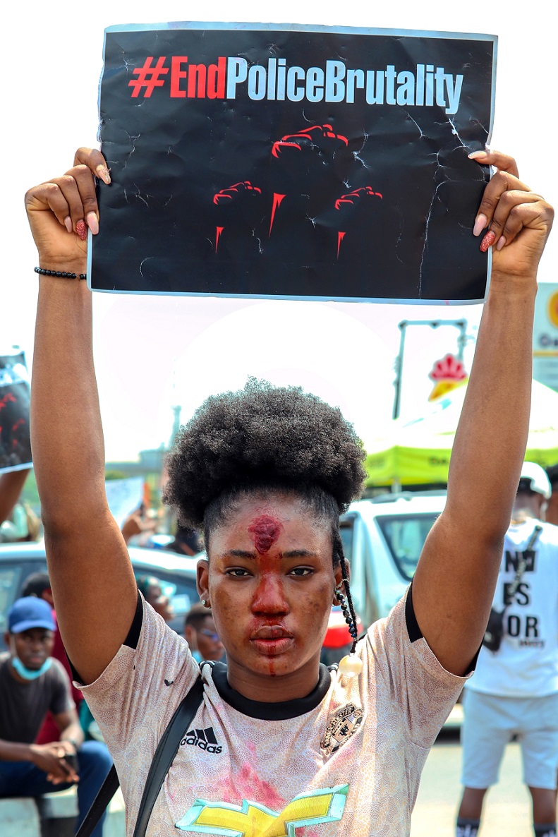 A woman holds a protest sign which reads, "End Police brutality."
