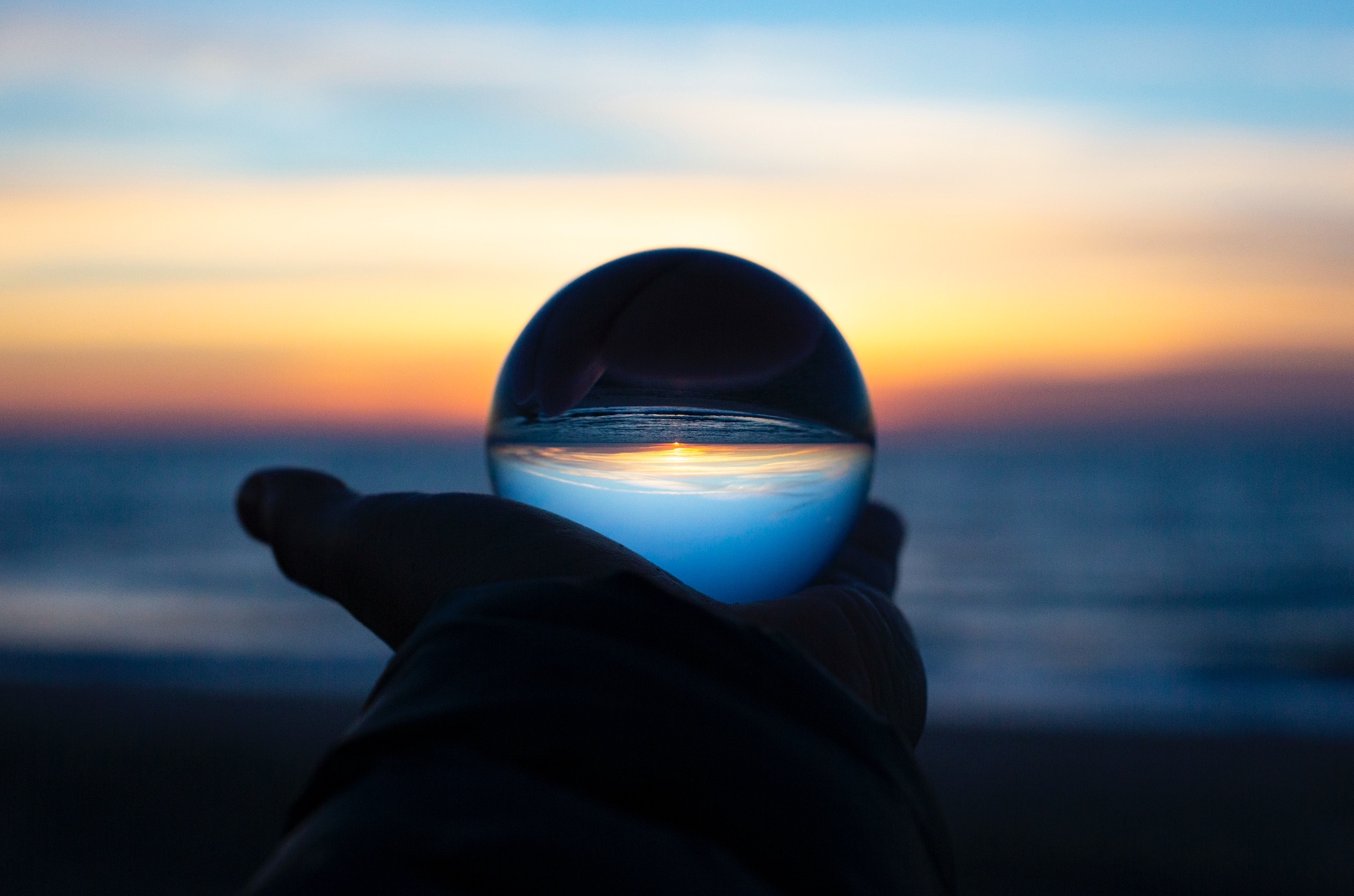 Person holding crystal ball against multicolored background; image by Drew Beamer, via Unsplash.com.