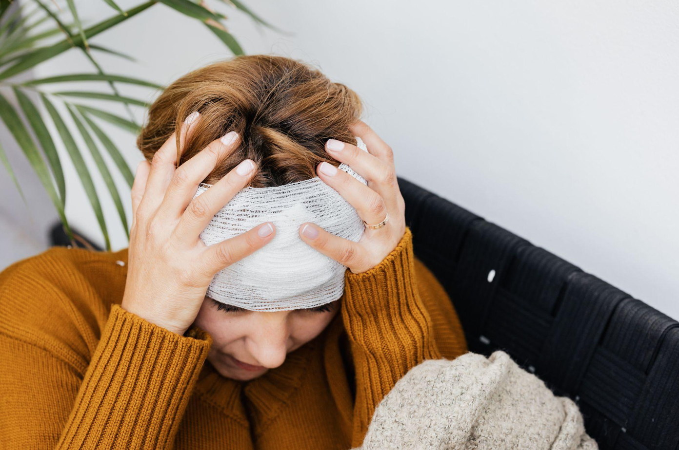 Woman holding her bandaged head; image by Karolina Grabowska, via Pexels.com.