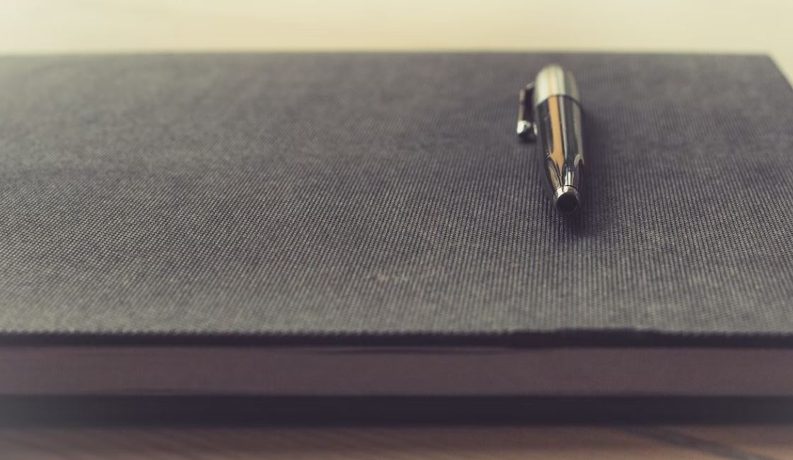 Pen and notebook on desk; image by Thomas Martinsen, via Unsplash.com.