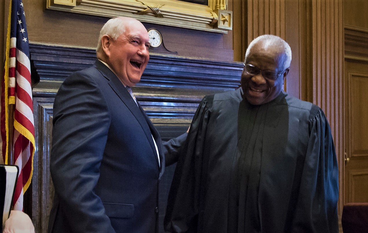 Clarence Thomas in judicial robe with Sonny Perdue in front of a fireplace.