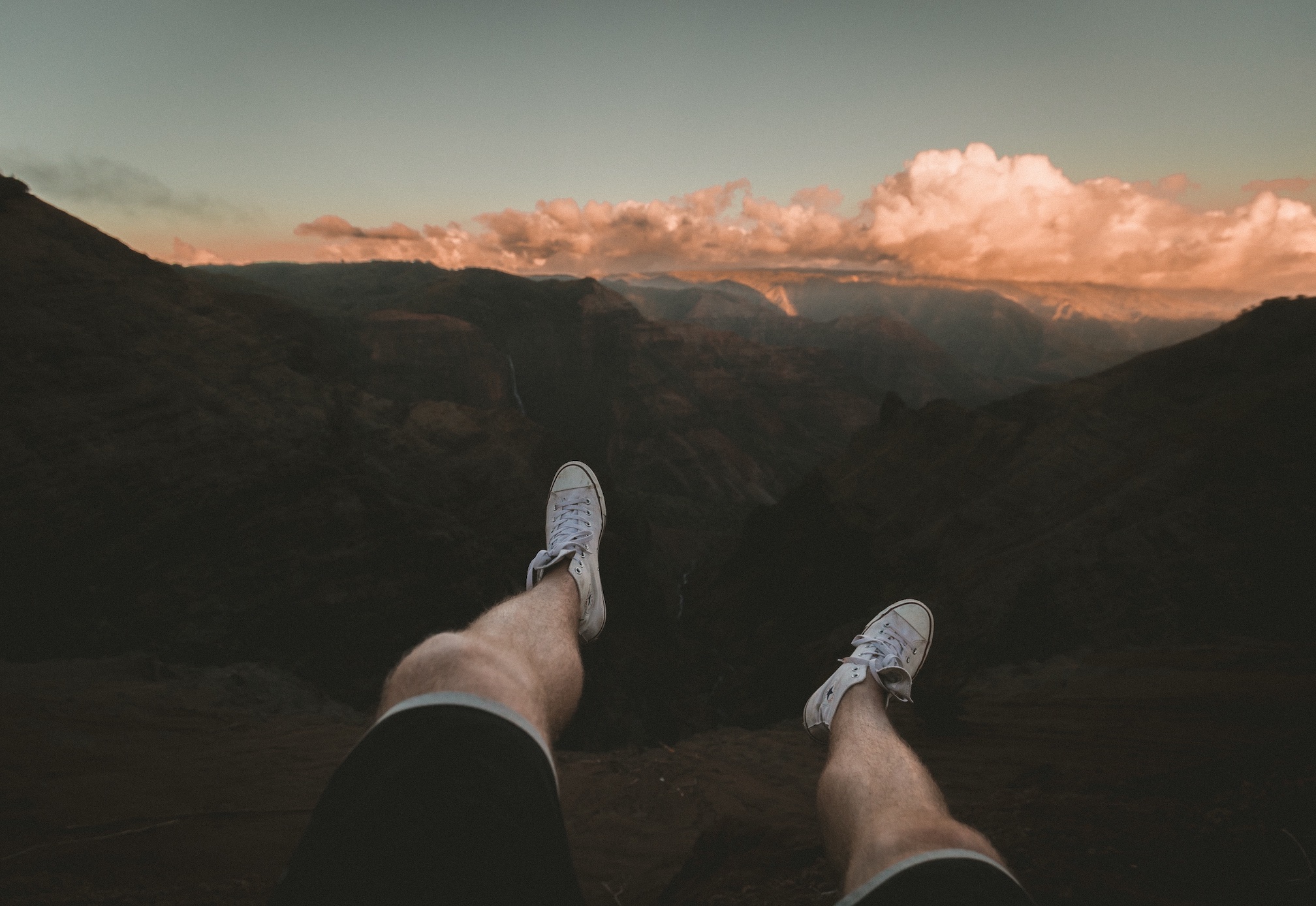 Man dangling legs over the edge of a canyon; image by Jakob Owens, via Unsplash.com.