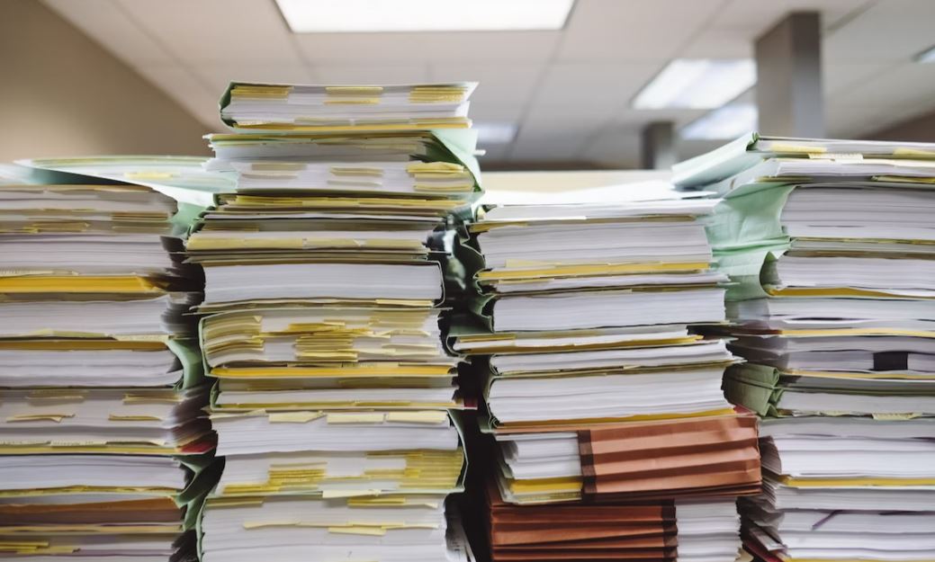 Stacks of books and papers; image by Wesley Tingey, via Unsplash.com.