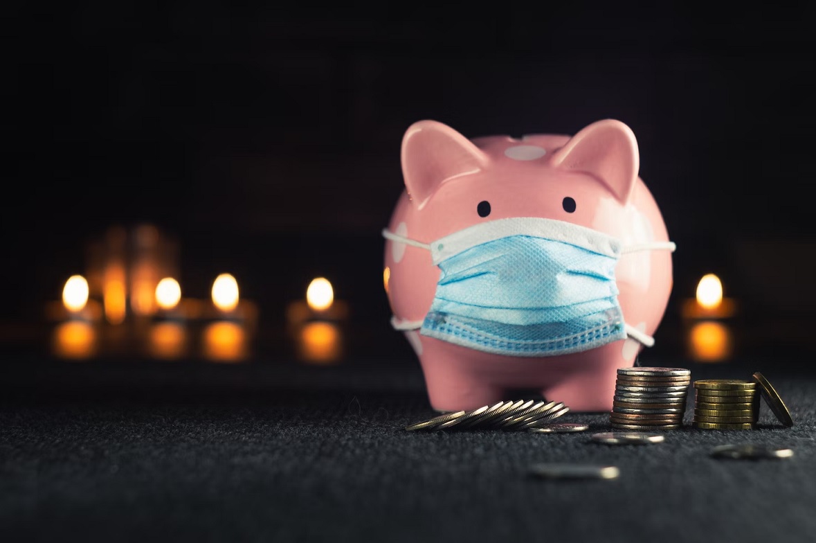 A piggy bank wearing a medical mask. There are some coins around it.