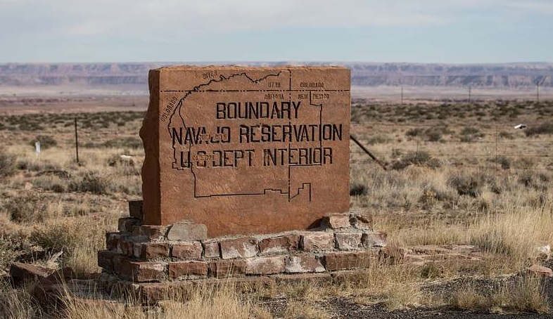A carved marker in a desert landscape reads "Boundary Navajo Reservation, U.S. Dept. Interior".