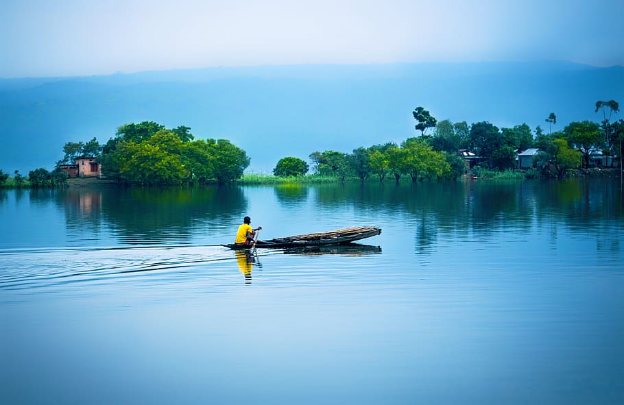 A person on a low boat skims the surface of a watery landscape.