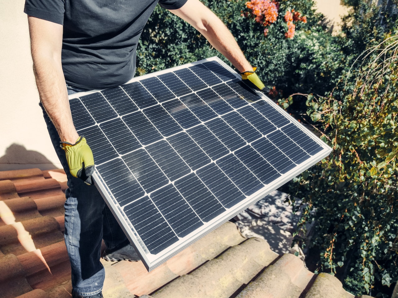 Man in black t-shirt holding a solar panel; image by Kindel Media, via Pexels.com.