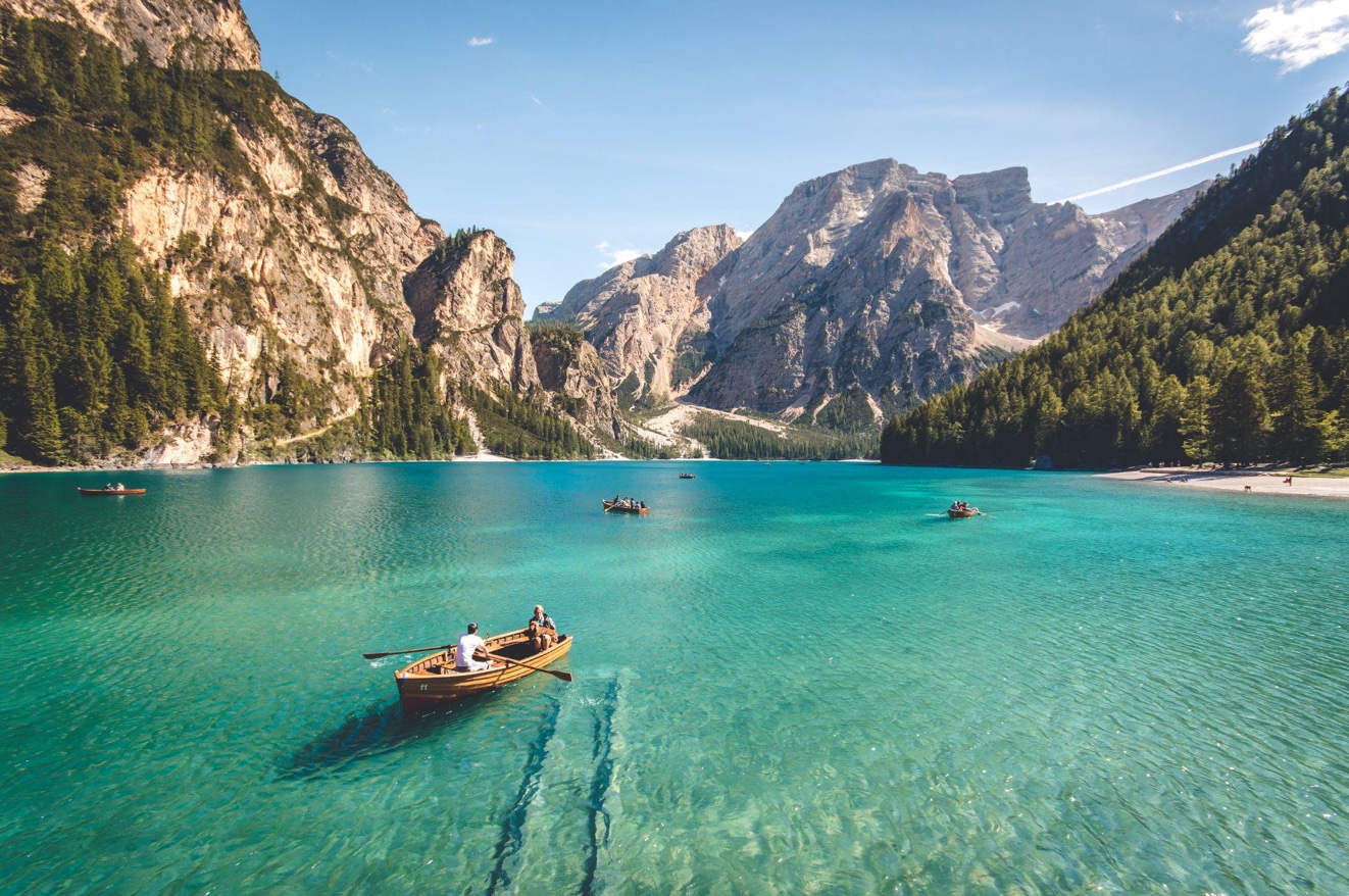 People boating on clear lake, mountains in background; image by Pietro De Grandi, via Unsplash.com.
