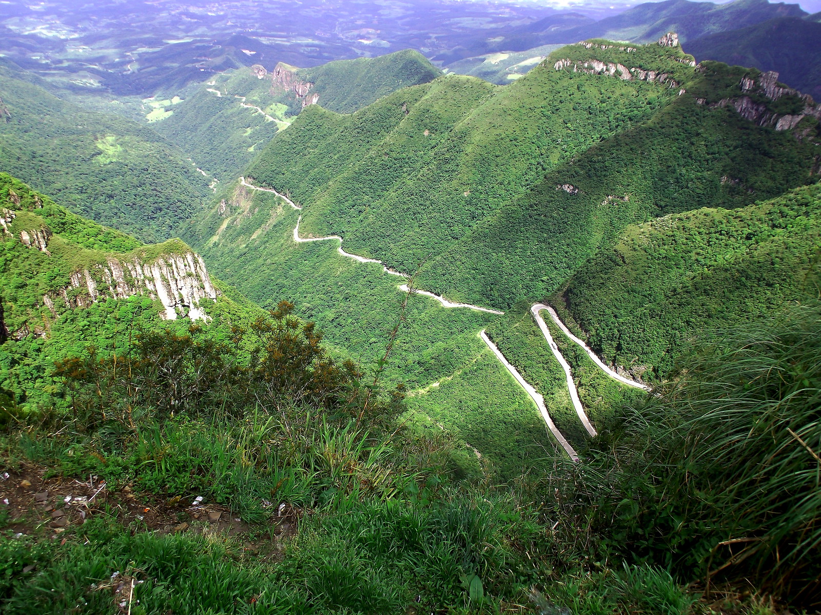 A long, winding road cuts through verdant, mountainous forest.