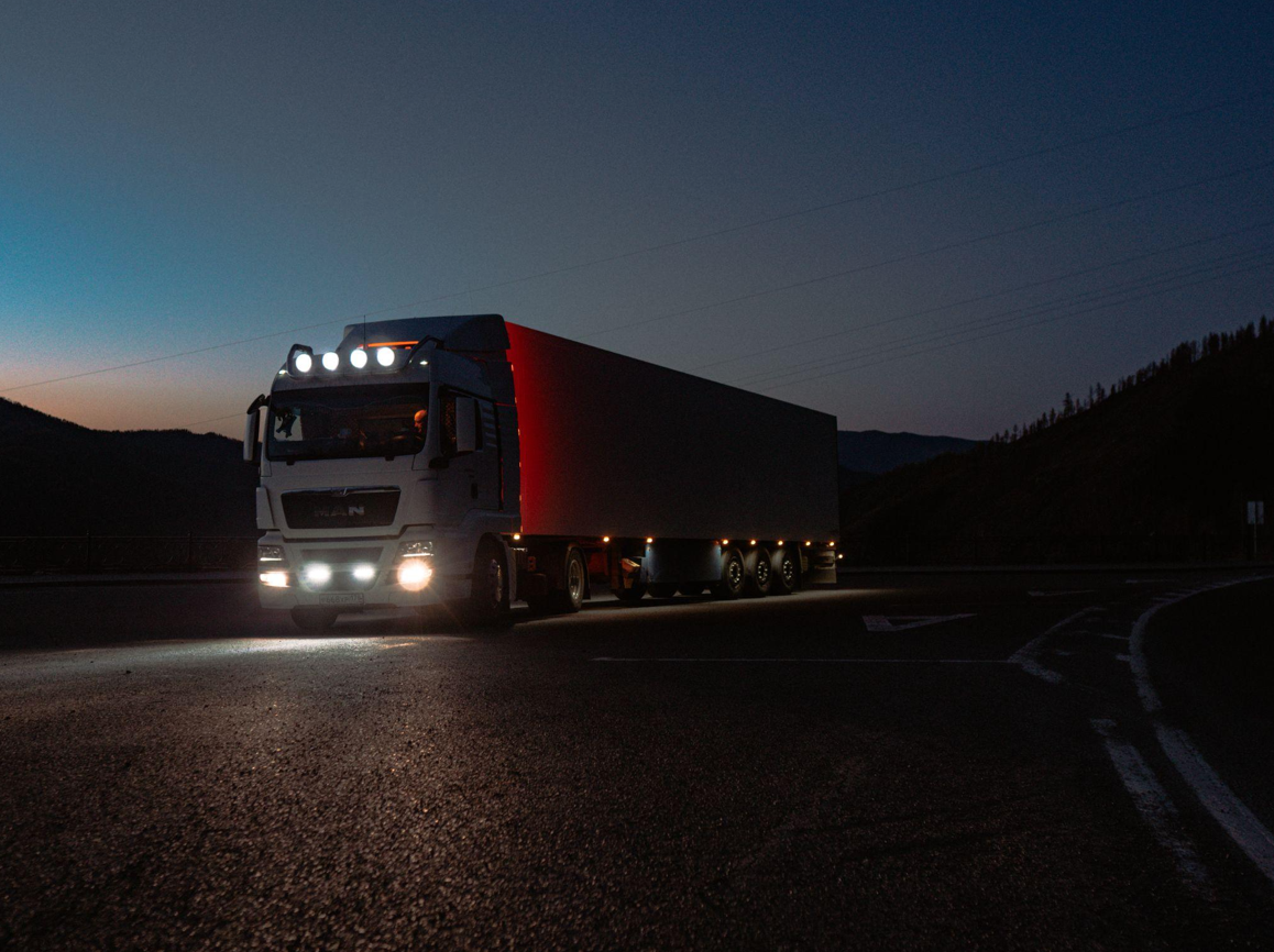 Semi-truck on the road with lights on at night; image by Screen 42, via Pexels.com.