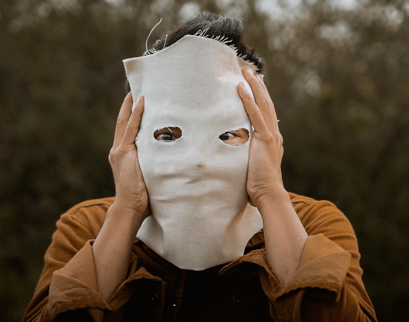 A person holds a creepy, blank mask in front of their face.