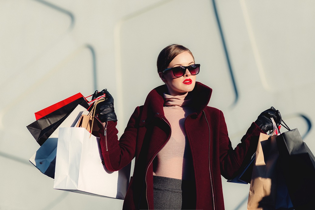 A caucasian woman in sunglasses holds a multitude of shopping bags in a carefree way.