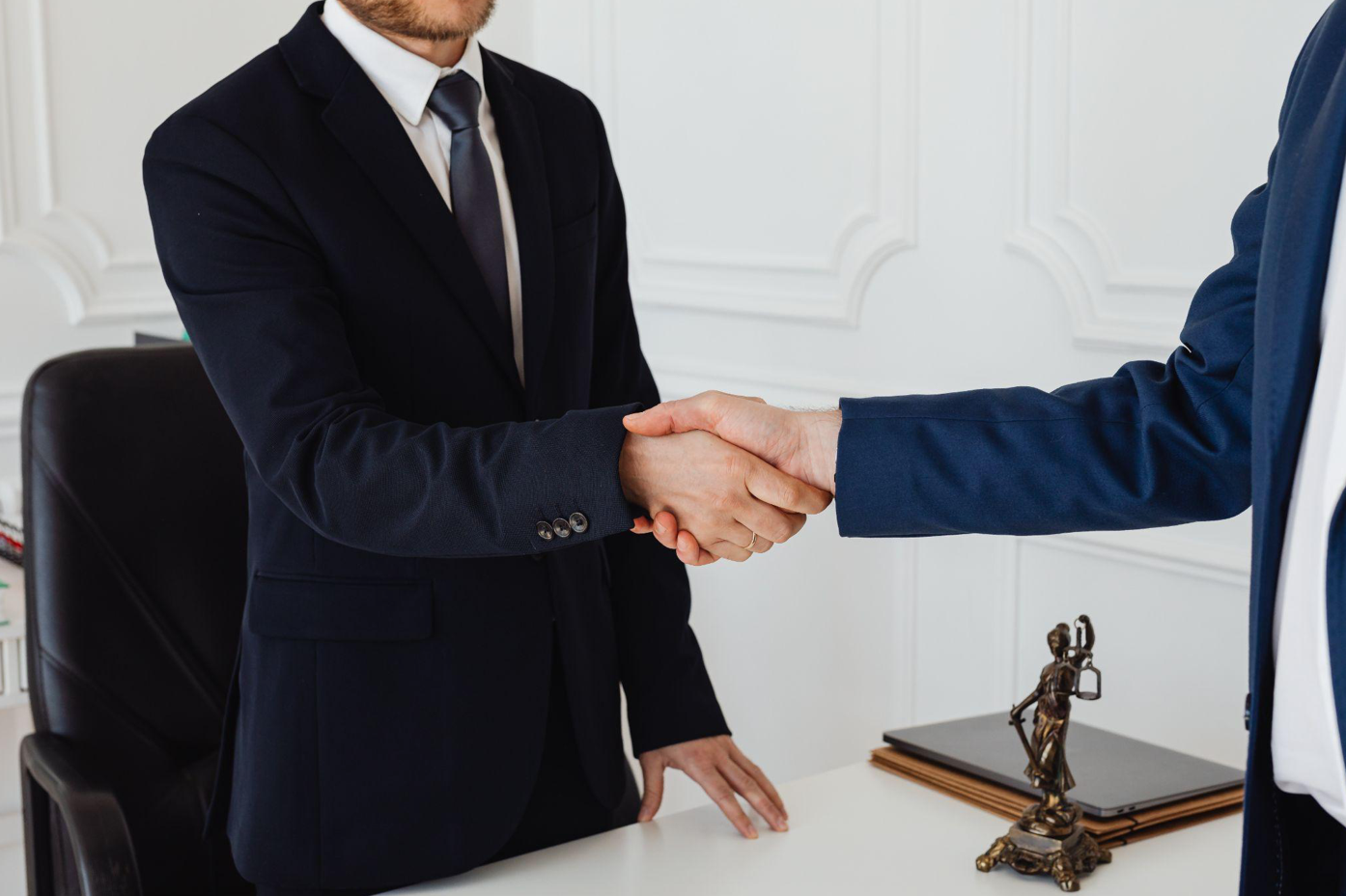 Two men in suits shaking hands over a desk; image by Karolina Grabowska, via Pexels.com.