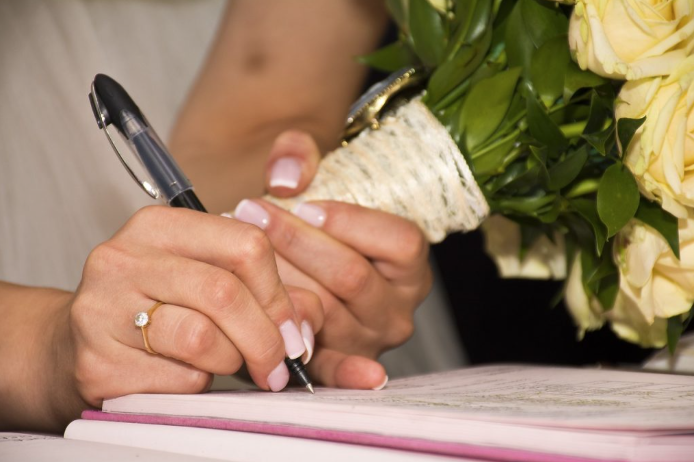Woman signing paper while holding bouquet; image by epicioci, via Pixabay.com.