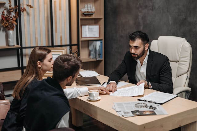 Man in black suit talking to his clients; image by Pavel Danilyuk, via Pexels.com.