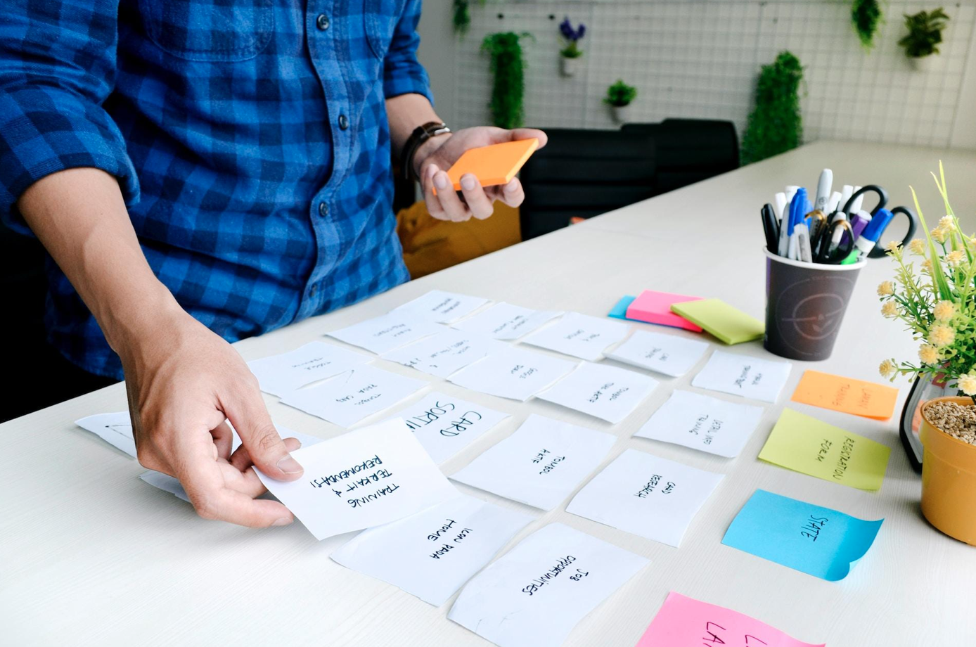 Man standing at counter reviewing post-it notes; image by UX Indonesia, via Unsplash.com.