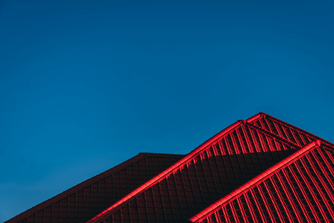 Deep red roof against a blue sky; image by Robin Kutesa, via Unsplash.com.