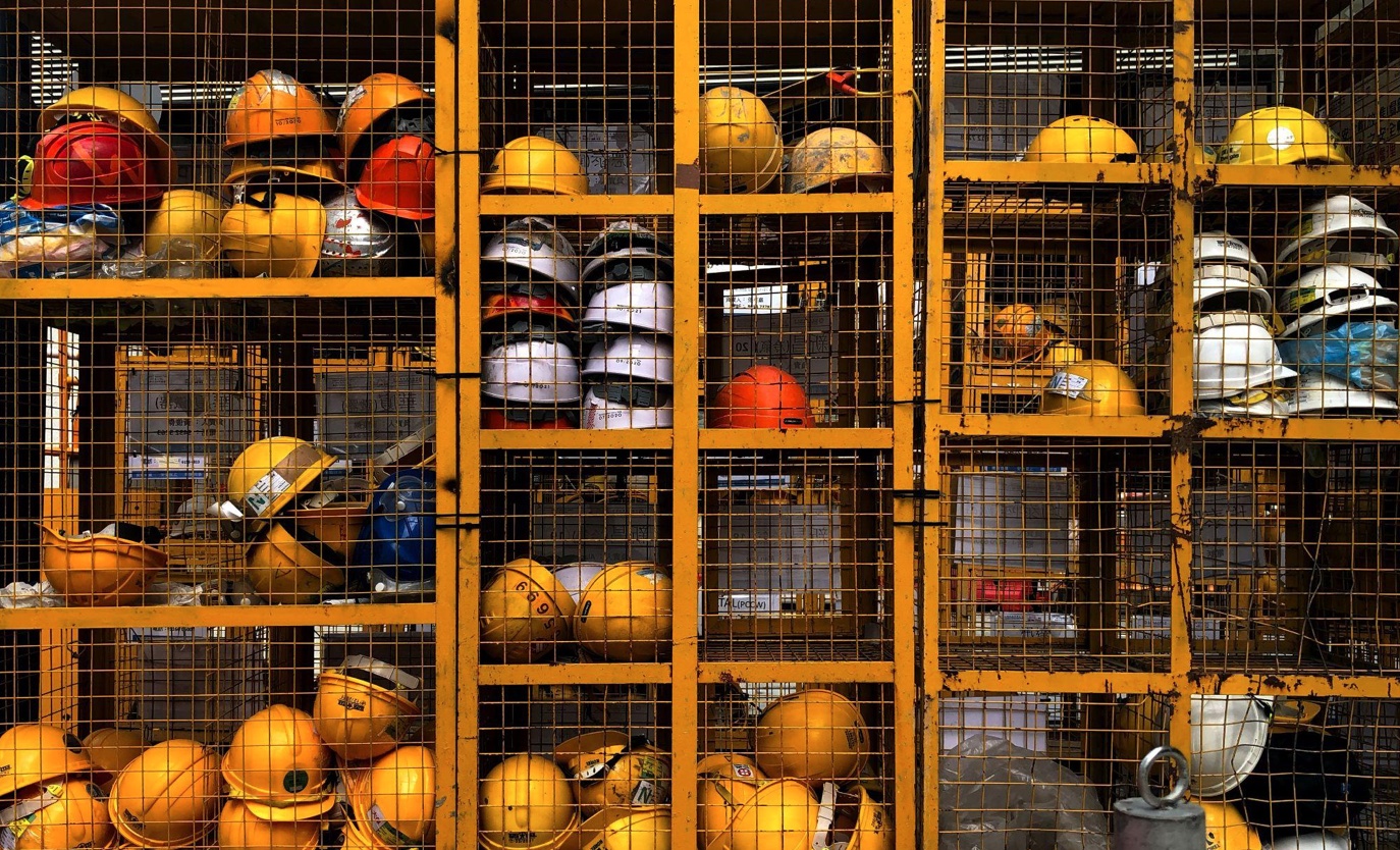 Rack full of yellow hard hats; image by Pop & Zebra, via Unsplash.com.