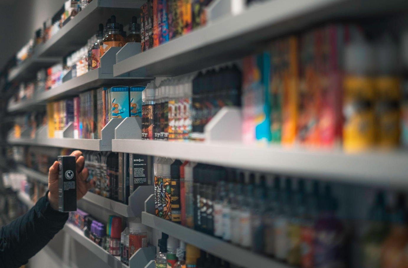 Woman in black shirt standing in front of store shelf of vape liquids; image by E-Liquids UK, via Unsplash.com.