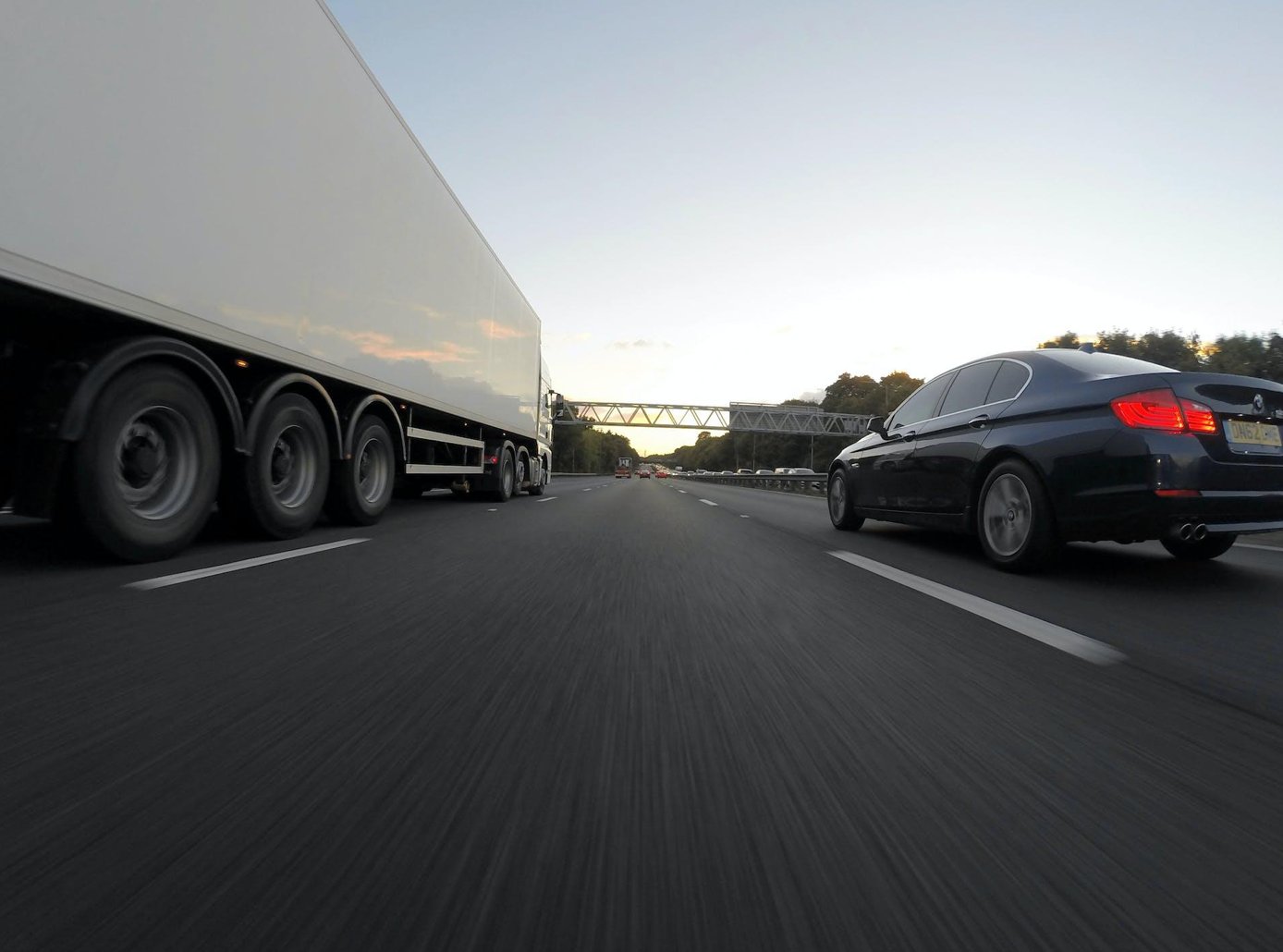 Blue Infiniti sedan on road with whith freight truck; image by Mike Bird, via Pexels.com.