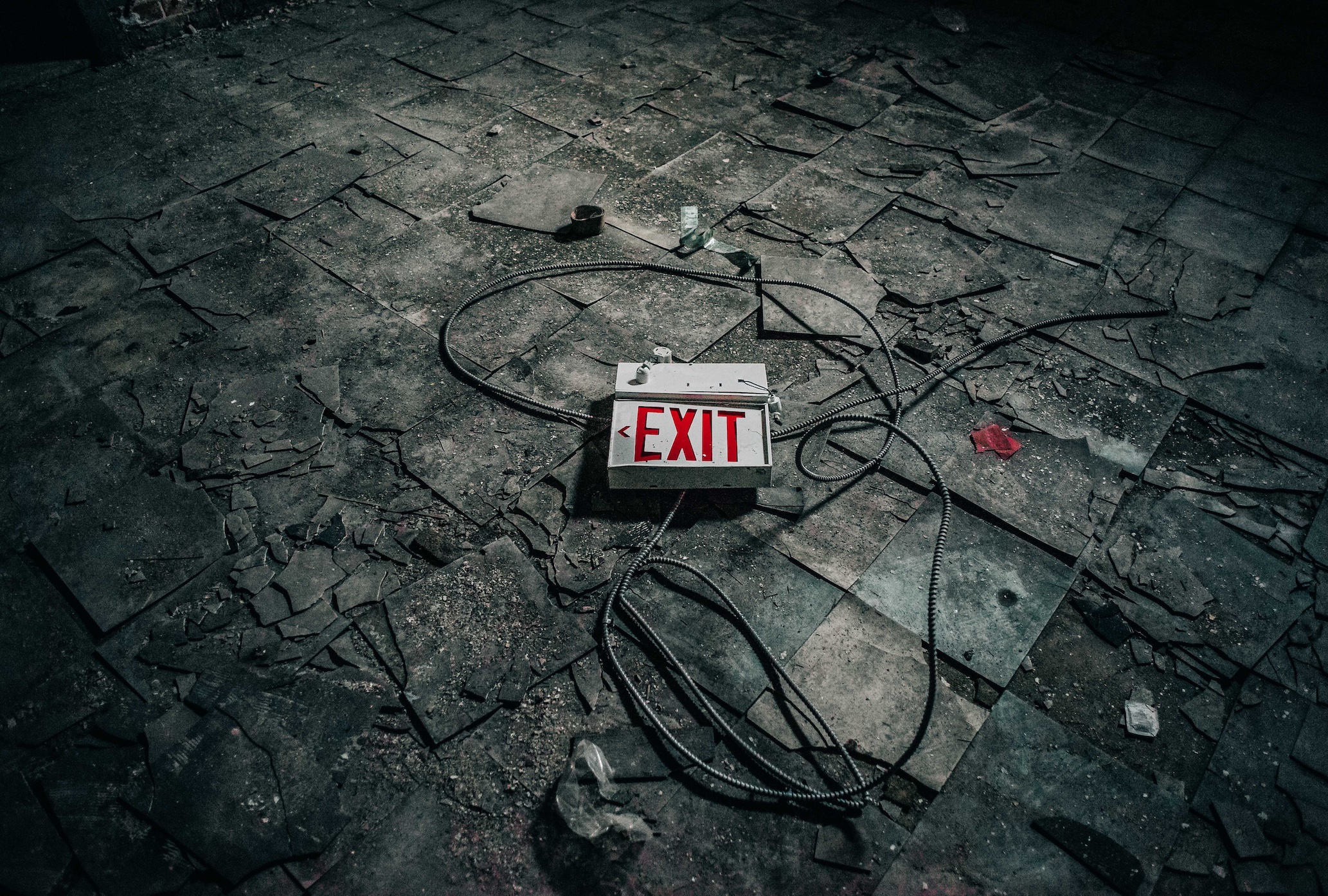 Damaged exit sign laying on floor in abandoned room; image by Kev Soto, via Unsplash.com.