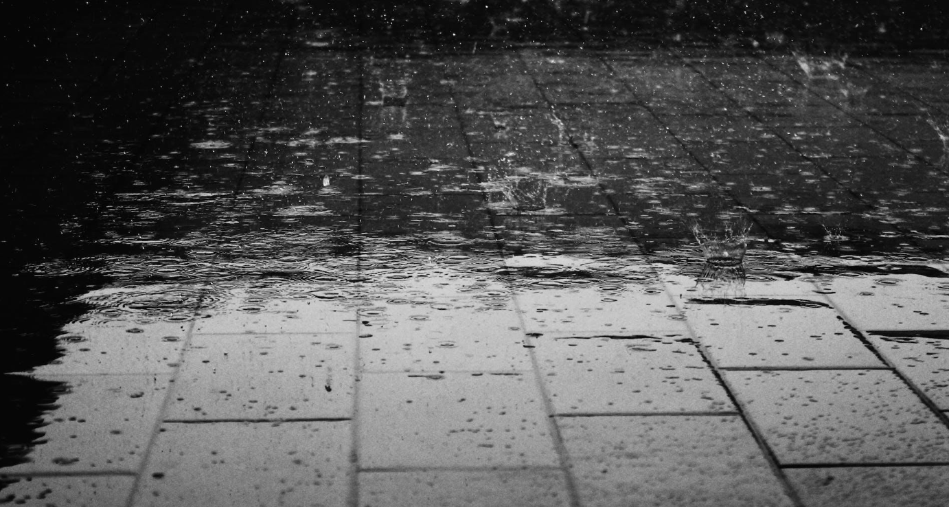 Grayscale shot of raindrops on brick pavers; image by Pixabay, via Pexels.com.