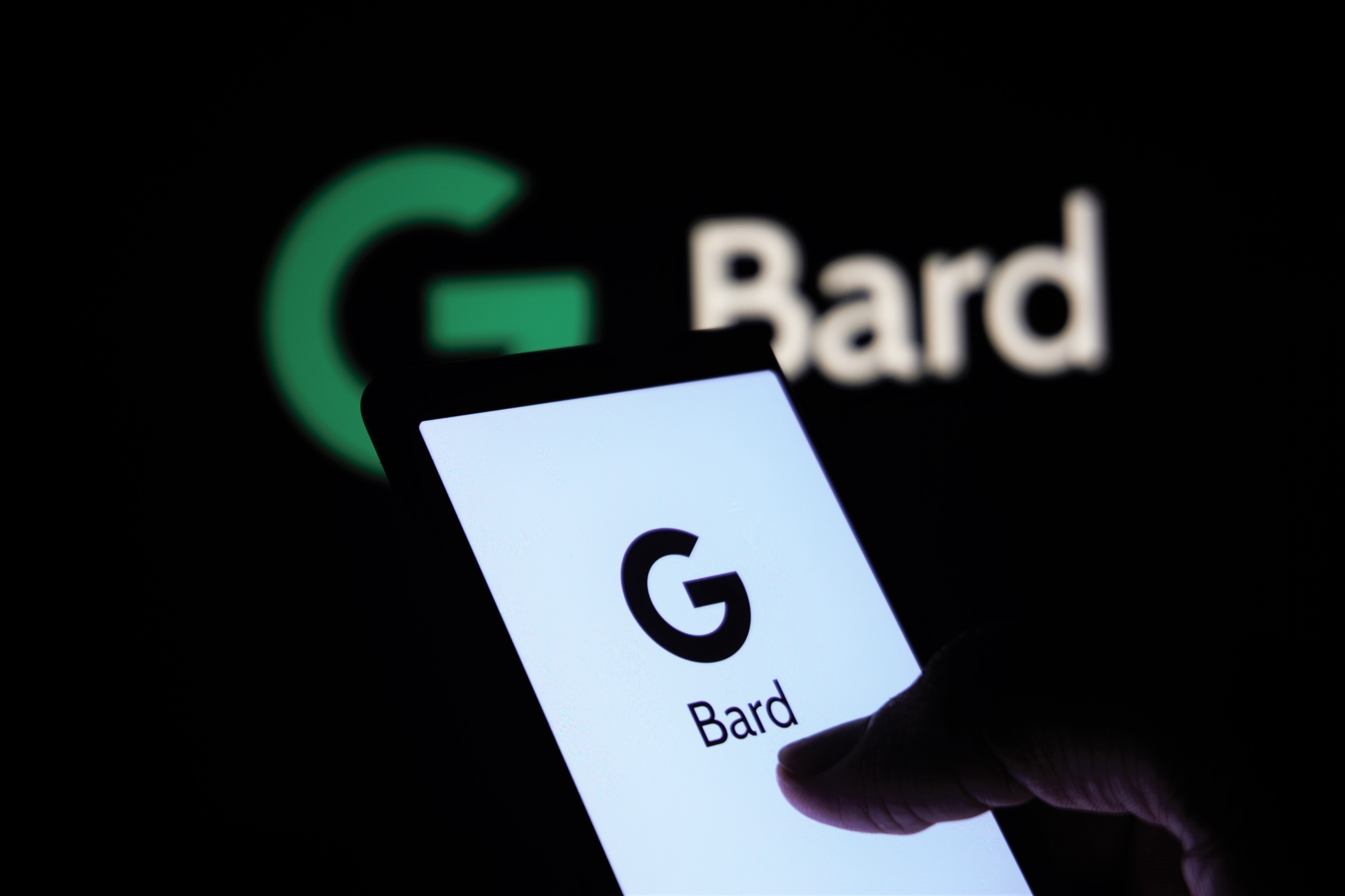 Man with smartphone that has G Bard on the sceen with G Bard sign as background; image by Mojahid Mottakin, via Unsplash.com.