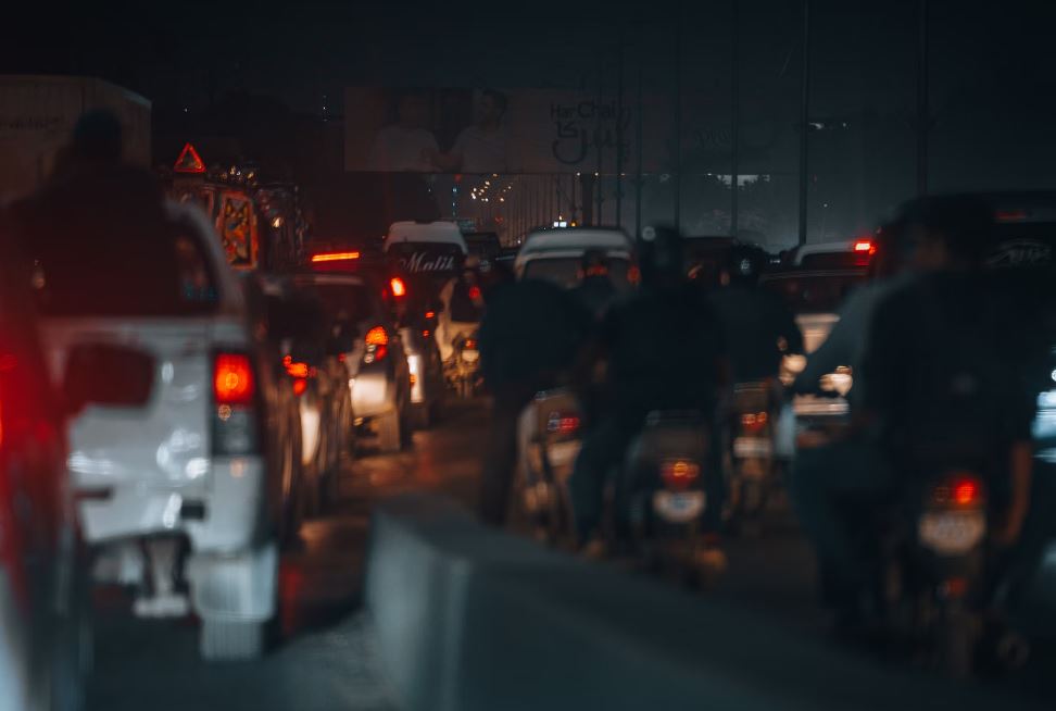 Group riding motorcycles at night in traffic; image by Tahamie Farooqui, via Unsplash.com.