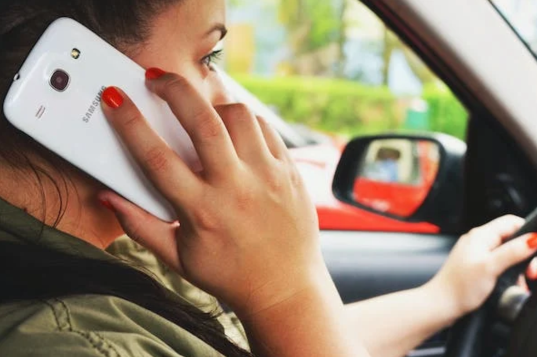 Woman driving while talking on cellphone; image by Breakingpic, via Pexels.com.