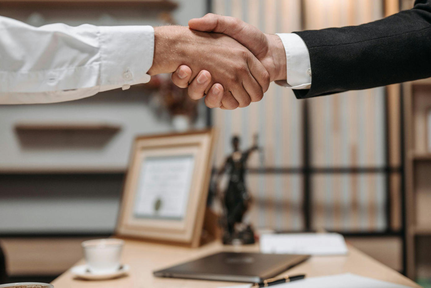 Client and lawyer shaking hands over lawyer's desk; image by Pavel Danilyuk, via Pexels.com.