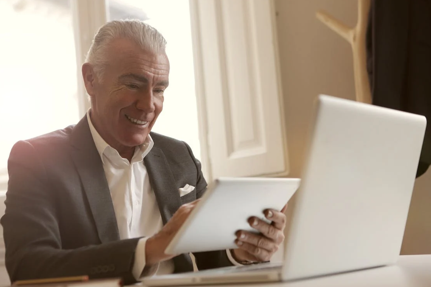 Older man using tablet and laptop; image by Andrea Piacquadio, via Unsplash.com.