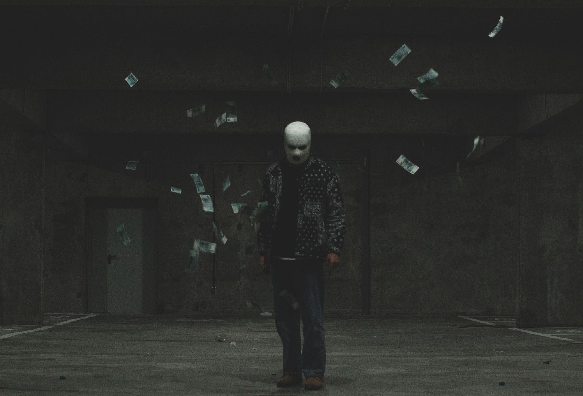 Masked man standing in dark room with paper money falling around him; image by Nikita Pavlov, via Unsplash.com.