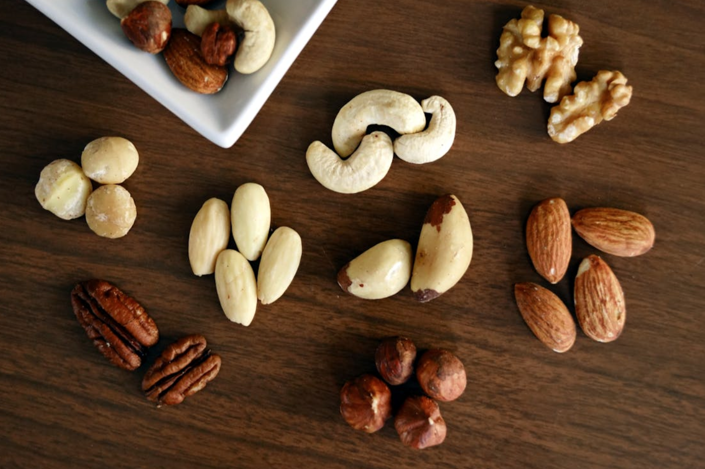Variety of brown nuts on a wooden table; image by Marta Branco, via Pexels.com.